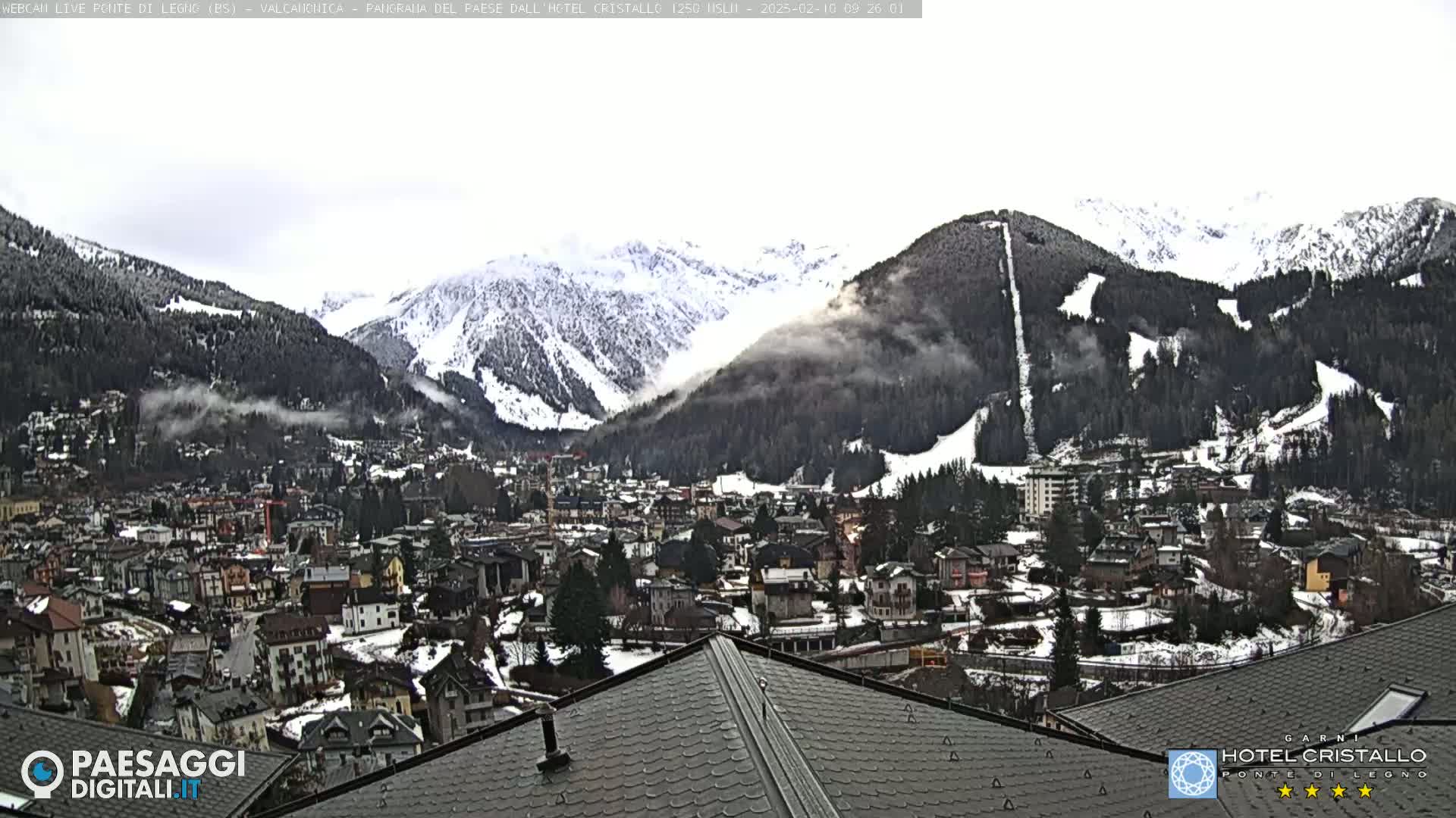 A snow-covered mountain town nestled in a valley beneath snow-capped mountains, with some fog or clouds in the valley.