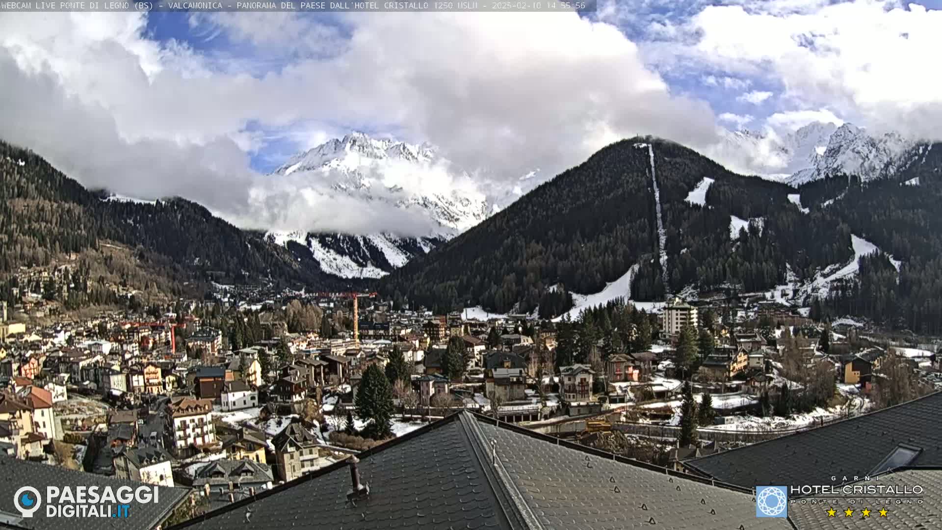 A partly cloudy day reveals a snow-dusted mountain range overlooking a town nestled in a valley.