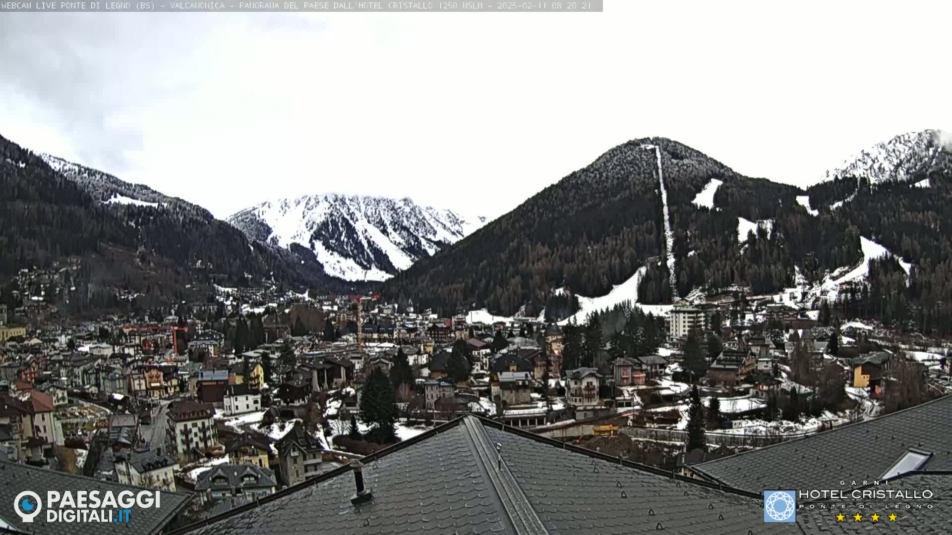 A snow-dusted mountain town nestled in a valley between snow-capped mountains under an overcast sky.