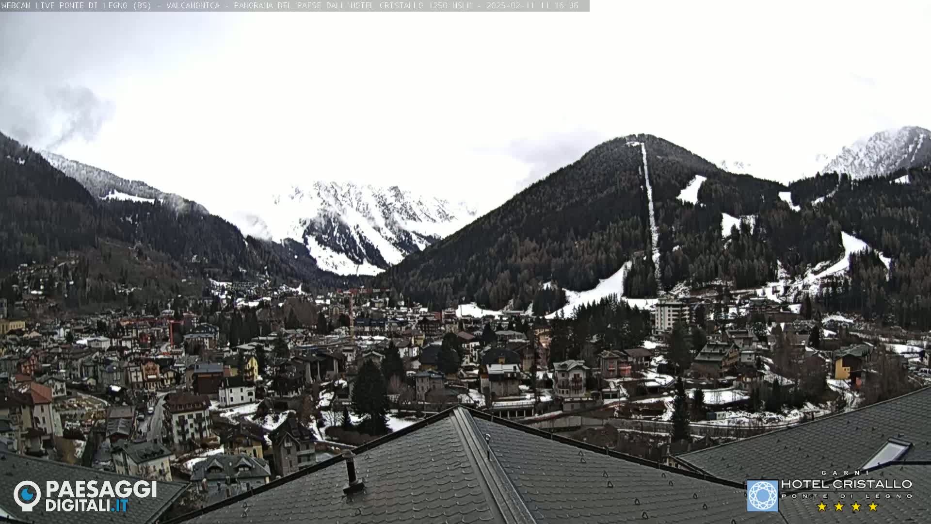 A snowy mountain village nestled in a valley between snow-covered mountains under an overcast sky.