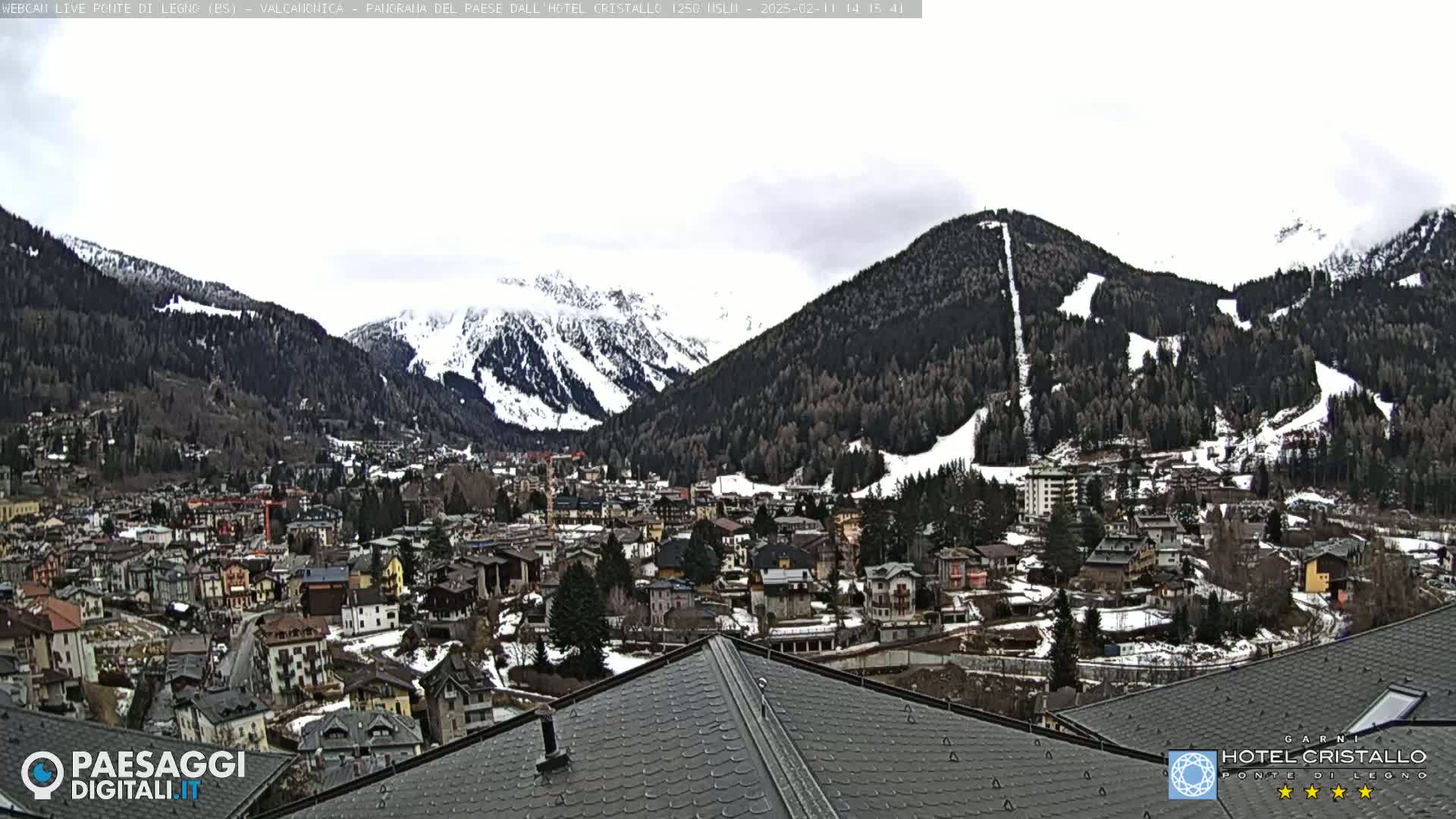 A snow-dusted mountain village nestled in a valley surrounded by snow-capped mountains under a cloudy sky.