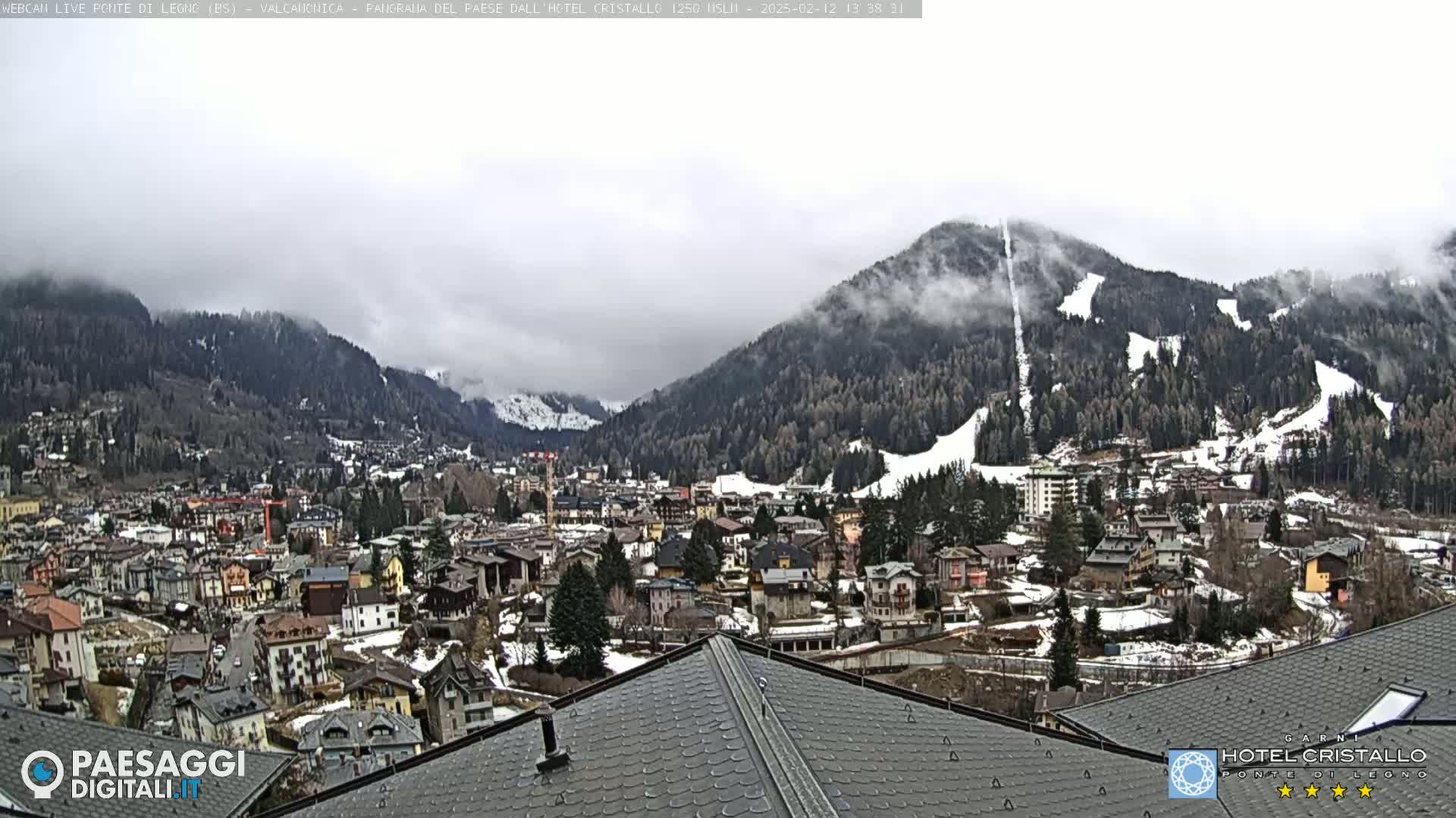 A mountain town nestled in a valley, partially obscured by fog, with snow-covered slopes visible in the background.