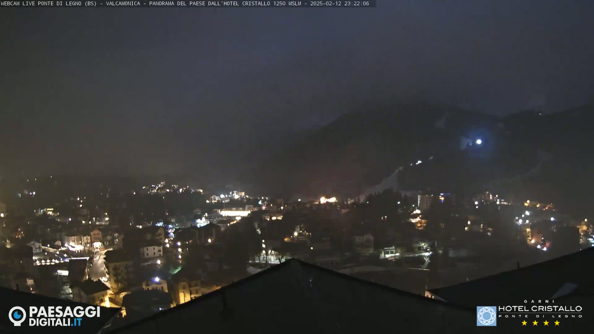 A nighttime view of a snow-covered town nestled in a mountain valley under a dark, overcast sky.