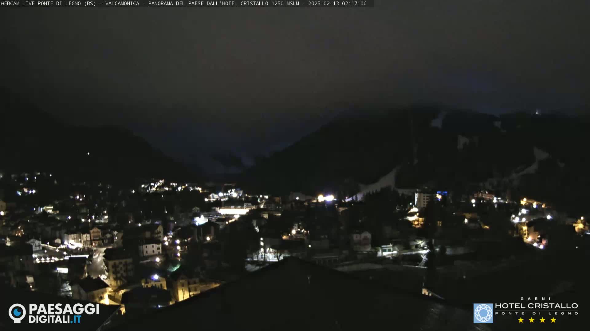 A nighttime view of a town nestled in a valley between dark mountains, under a mostly clear, dark sky.