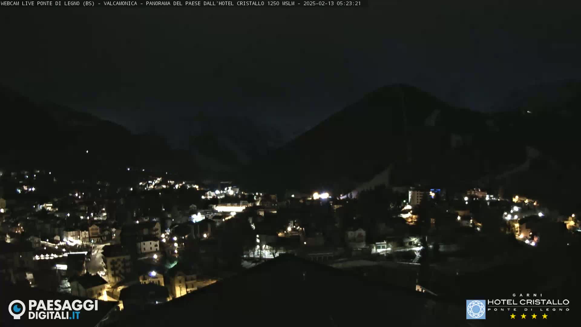 A nighttime view of a town nestled in a valley, surrounded by dark mountains under a clear, dark sky.