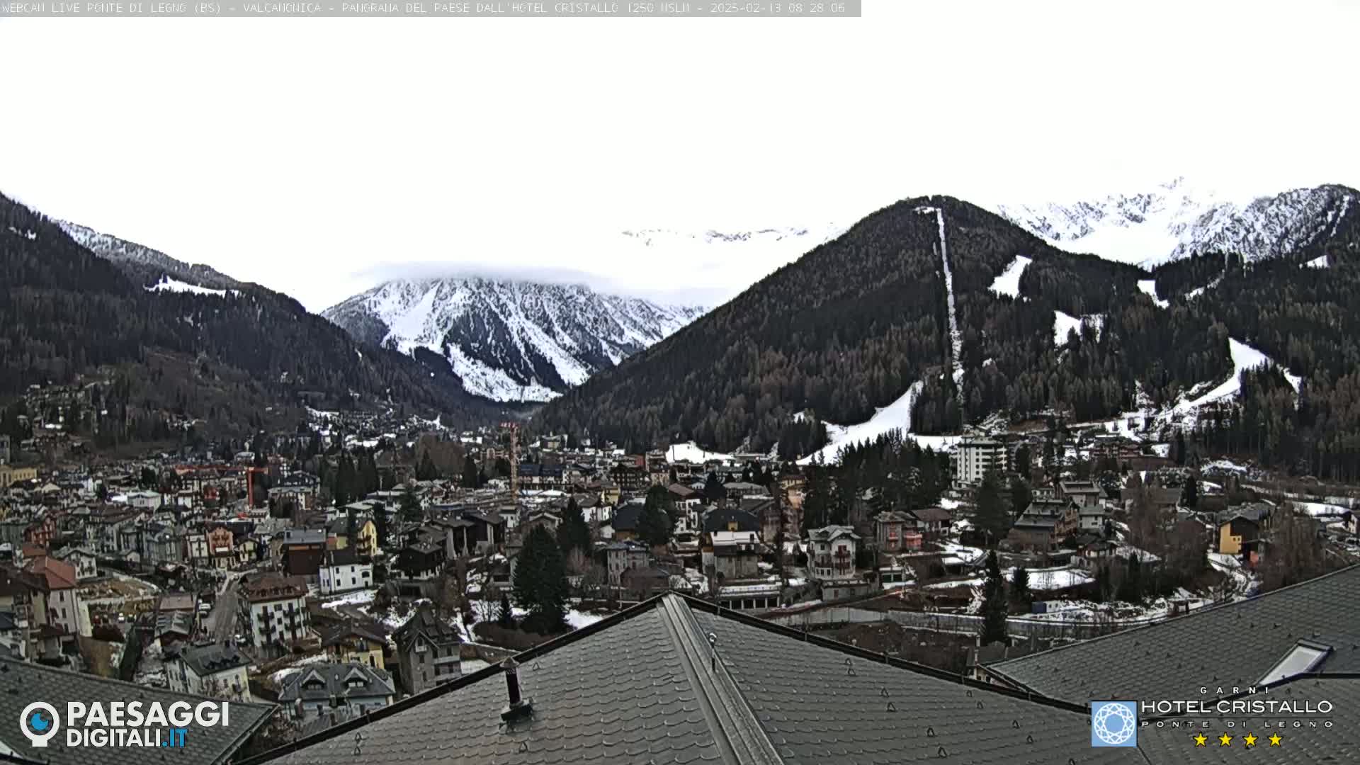A snow-dusted mountain town nestled in a valley between snow-capped mountains under an overcast sky.
