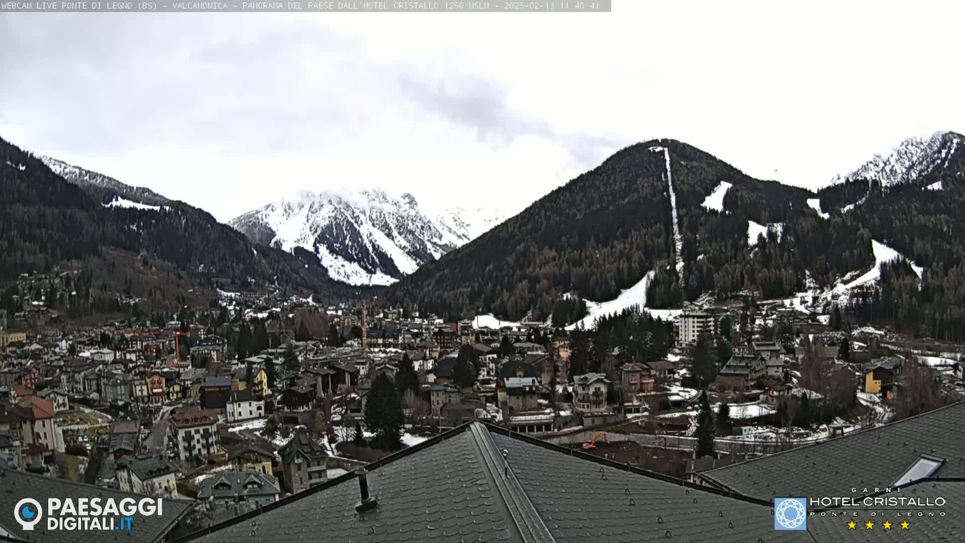 A snow-dusted mountain village nestled in a valley between snow-capped mountains under an overcast sky.