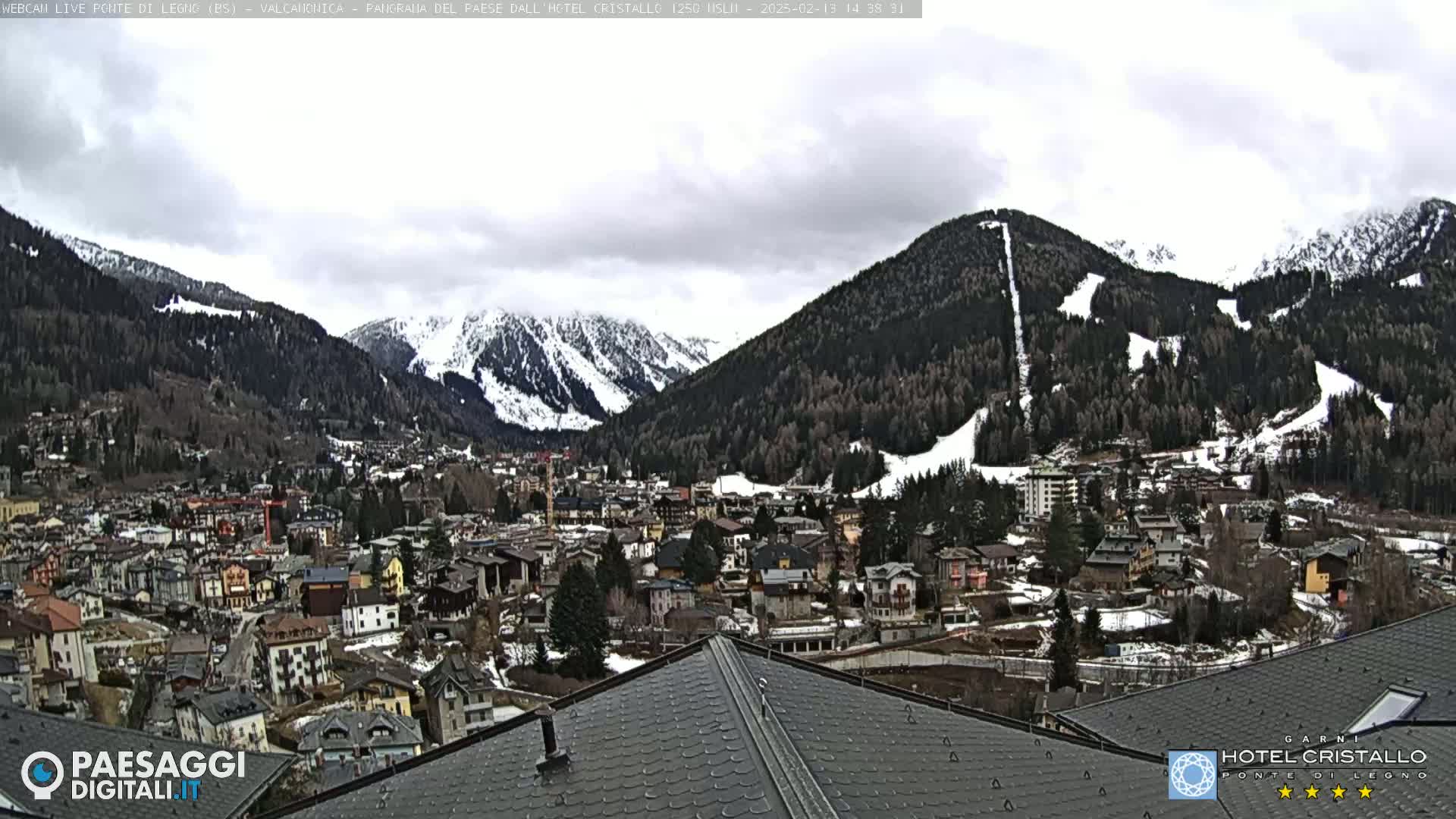 A mountain town nestled in a valley, with snow-capped mountains in the background under a cloudy sky.