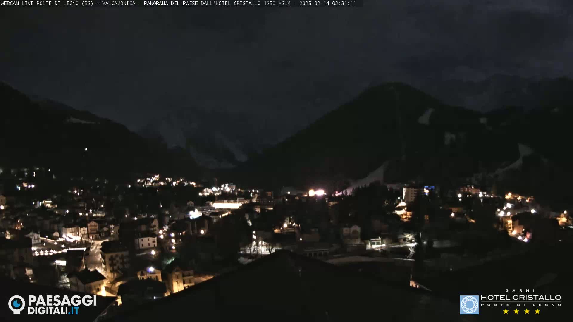 A nighttime view of a town nestled in a valley between dark mountains under a mostly clear sky.