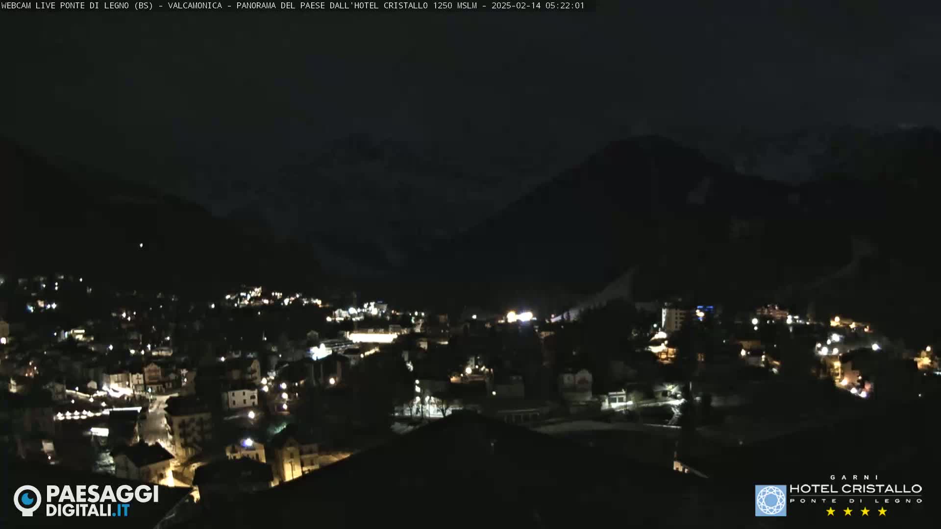 A nighttime view of a town nestled in a valley, surrounded by dark mountains under a clear, dark sky.