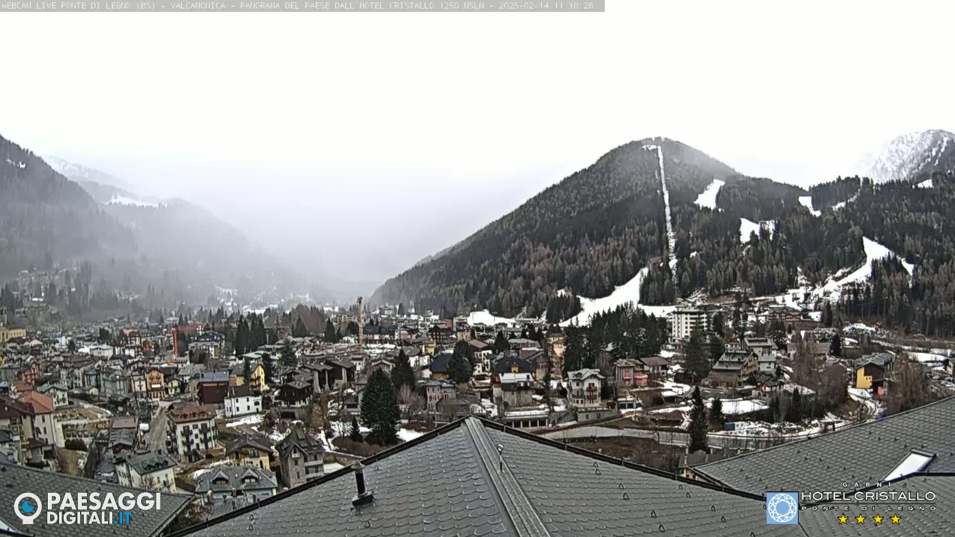 A hazy, overcast view of a snow-dusted mountainside overlooking a town nestled in a valley.