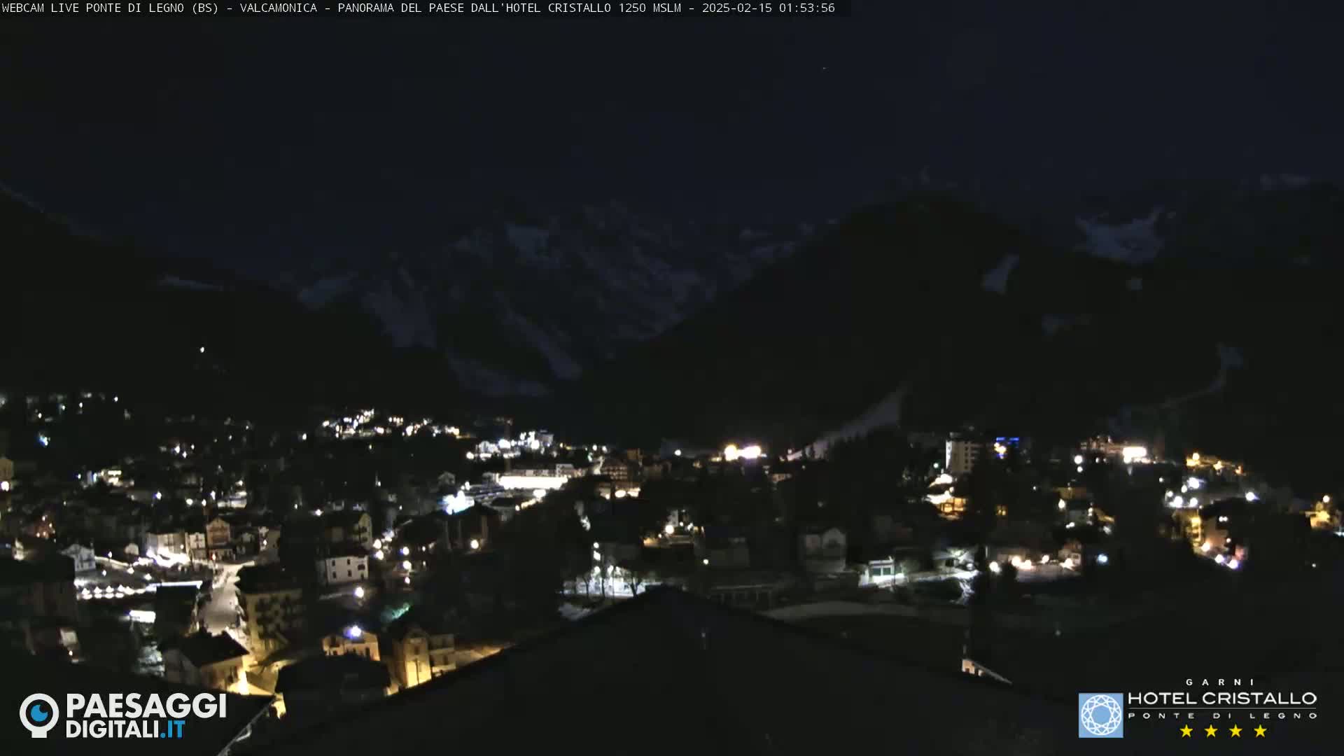 A nighttime view of a town nestled in a valley between dark mountains, illuminated by scattered lights.