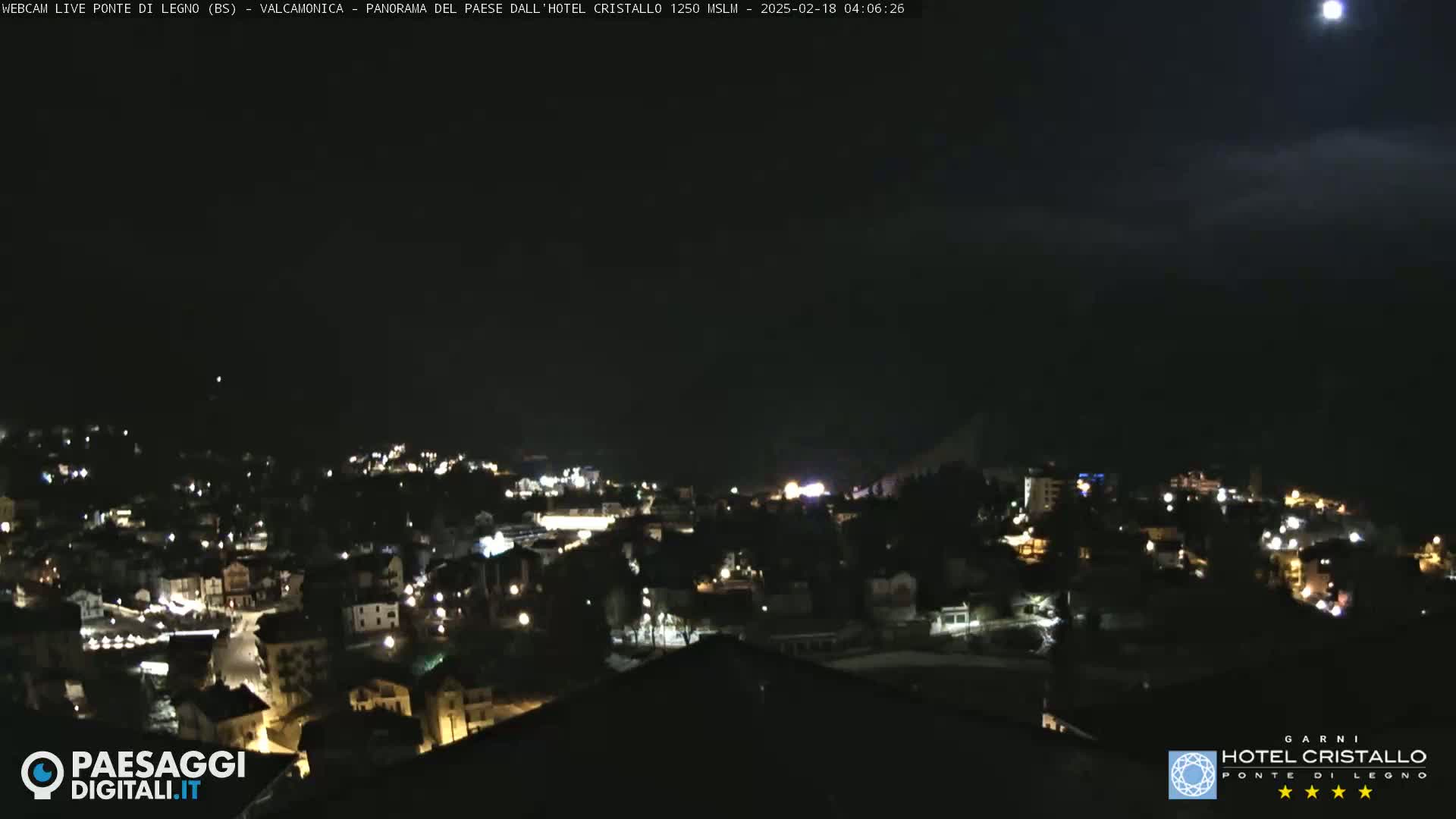 A nighttime, high-angle view of a town illuminated by lights under a mostly clear sky with a bright moon.