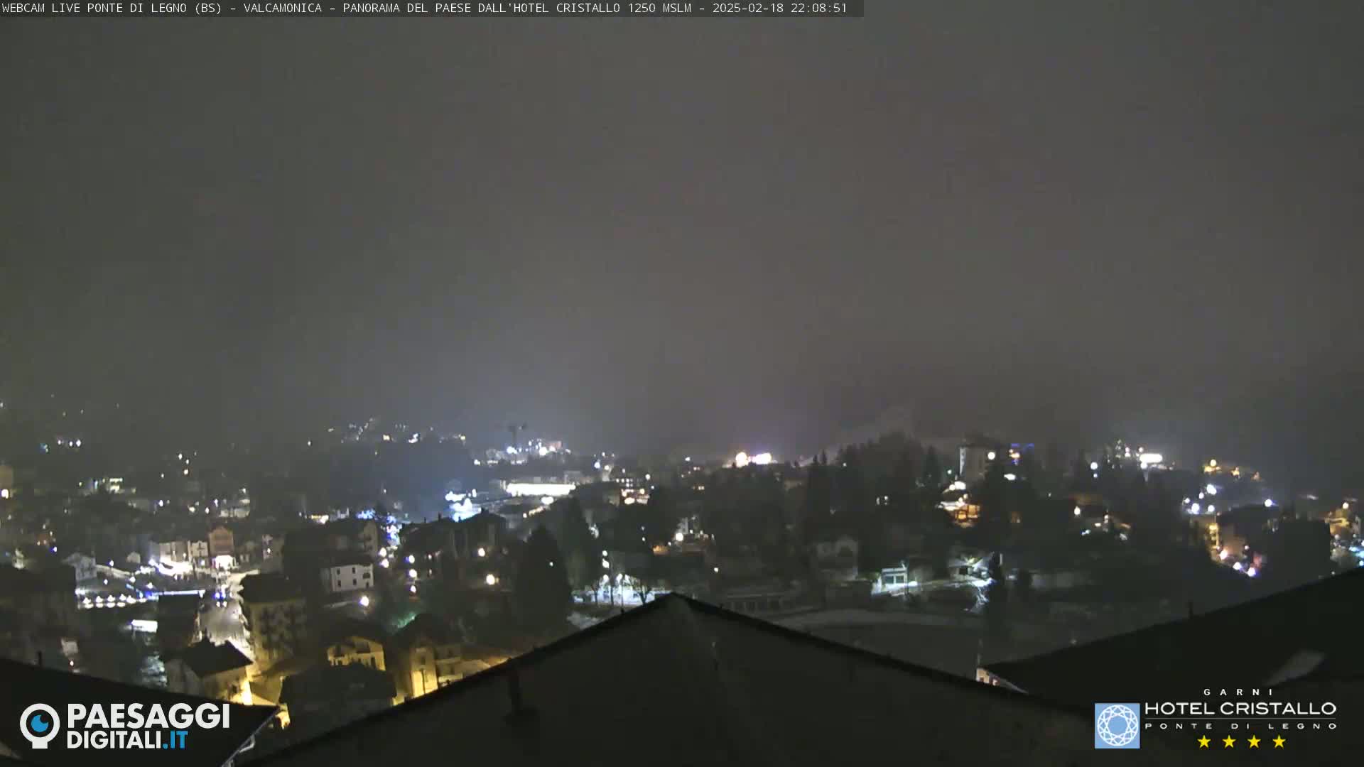 A nighttime view of a town nestled in hills under a hazy, dark sky.