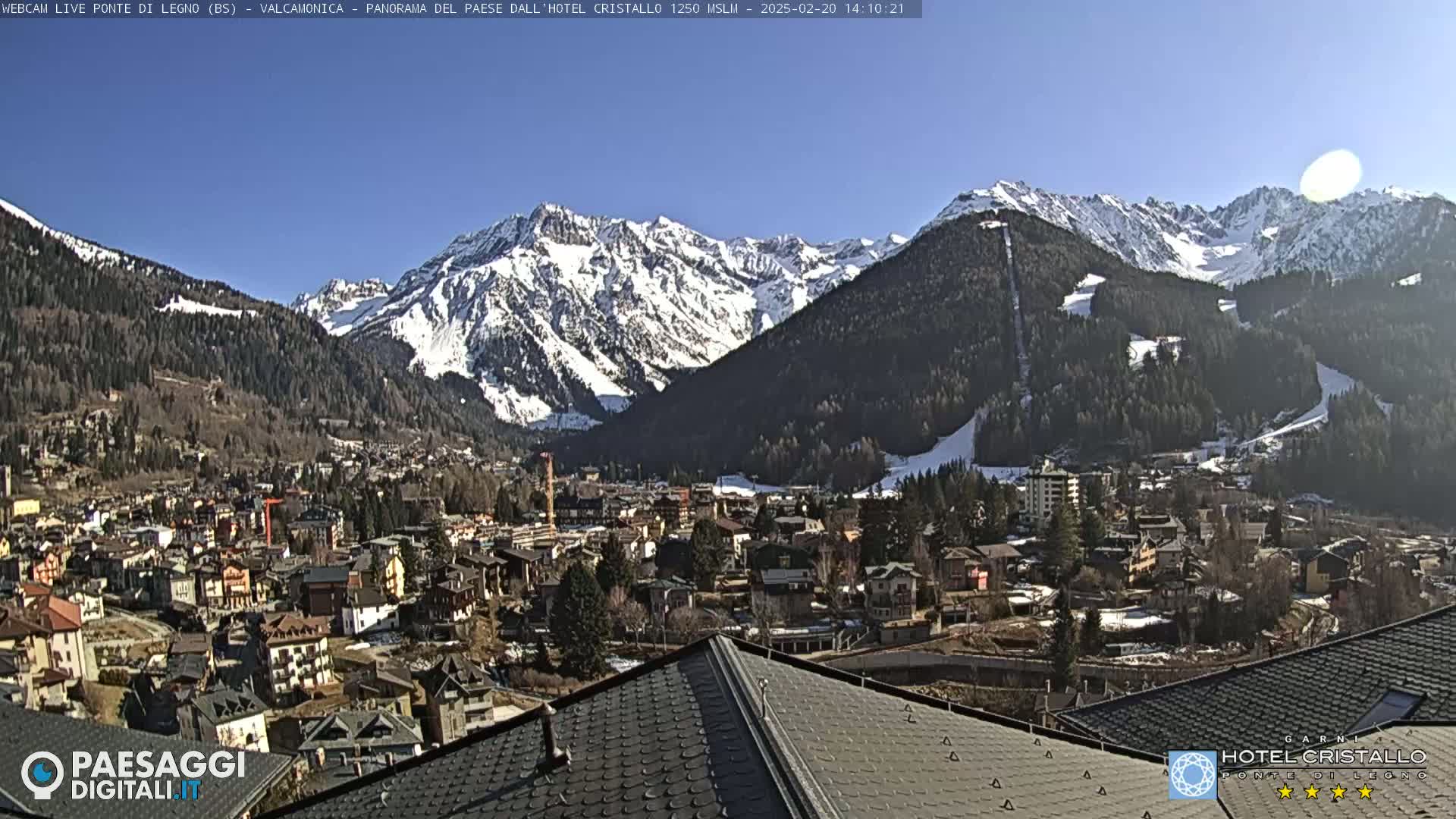 A sunny day reveals a snow-capped mountain range overlooking a town nestled in a valley.
