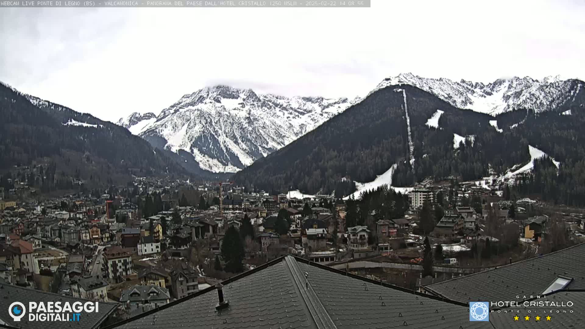 A snow-dusted mountain range overlooks a town nestled in a valley under an overcast sky.