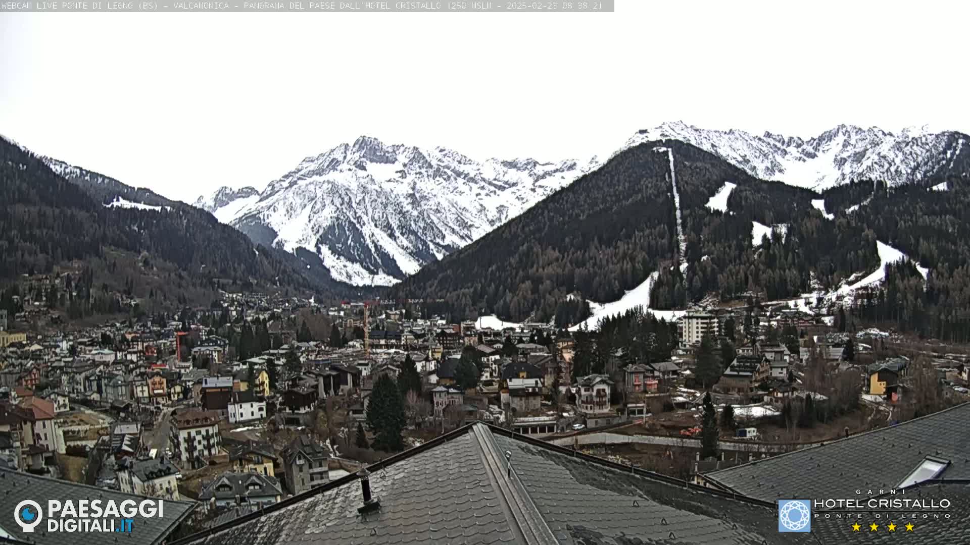 A snow-dusted mountain range overlooks a town nestled in a valley, viewed from a sloped roof.