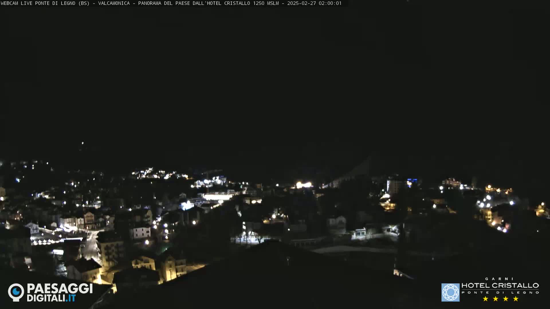 A nighttime, high-angle view shows a town's lights scattered across a hillside under a dark sky.