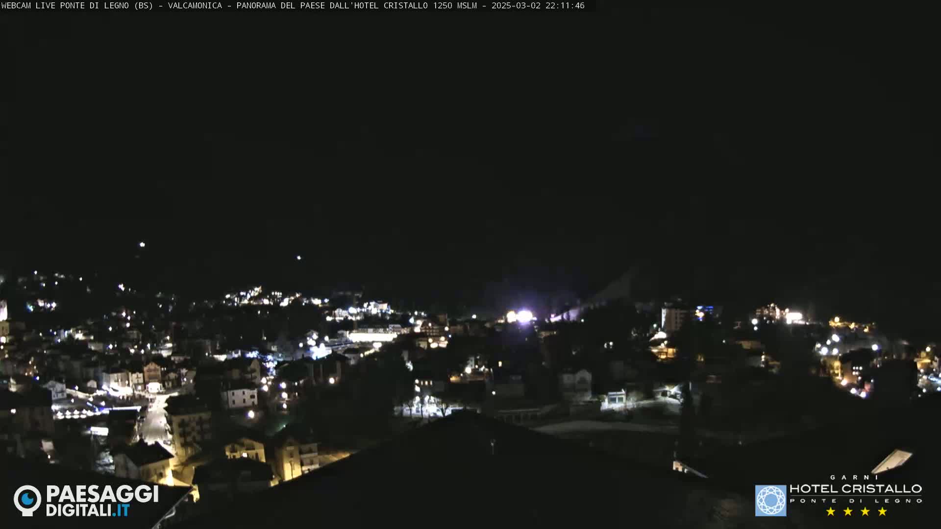 A nighttime, long shot of a town illuminated by lights against a dark sky.