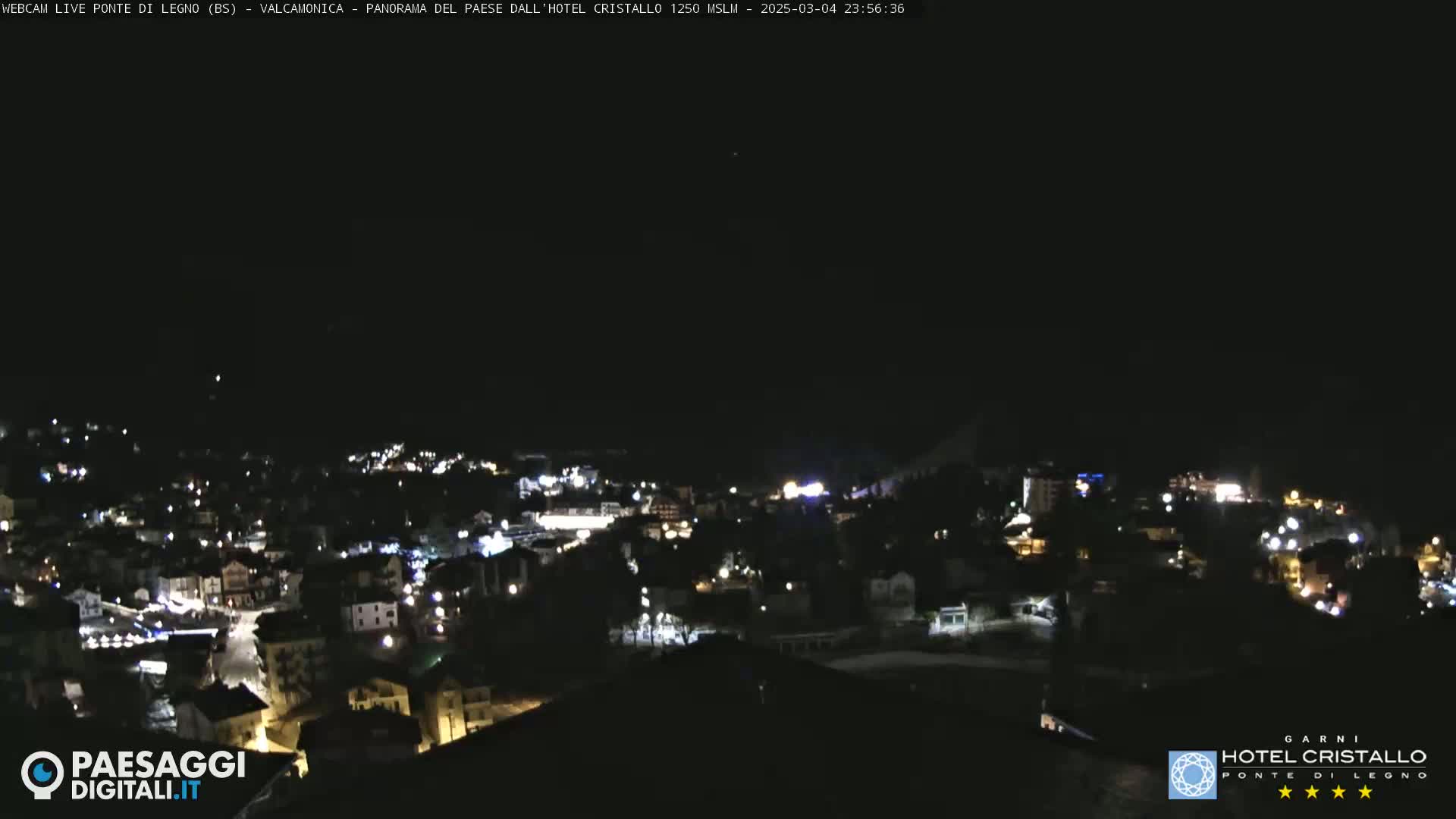 A nighttime, high-angle view shows a town's lights scattered across a hillside under a clear, dark sky.