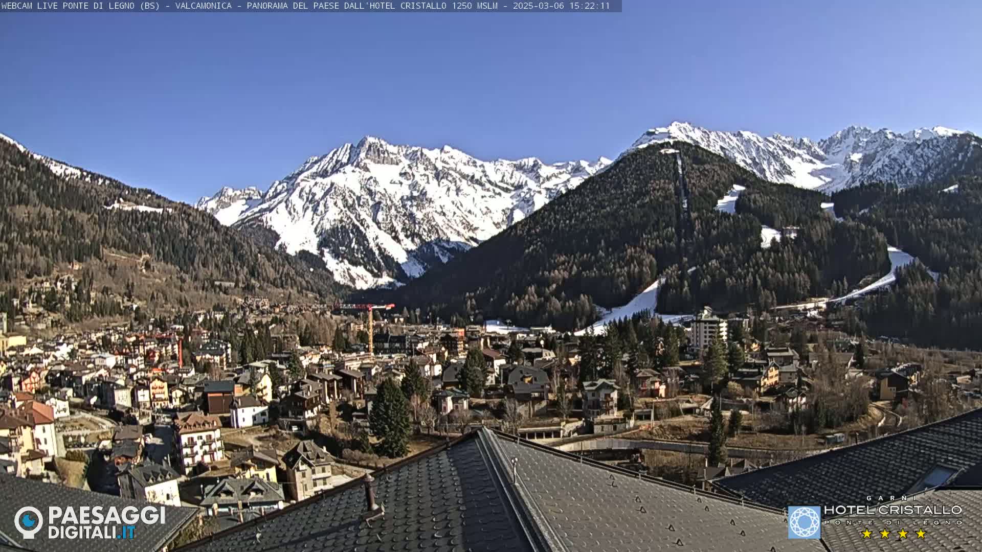 A snow-capped mountain range overlooks a town nestled in a valley on a sunny day.