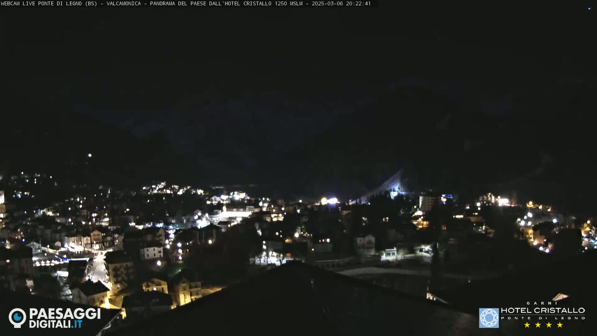 A nighttime, long shot of a town nestled in a valley, illuminated by scattered lights, under a clear, dark sky.