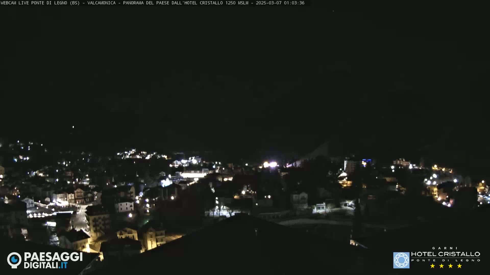 A nighttime, high-angle view of a town illuminated by scattered lights under a dark, clear sky.