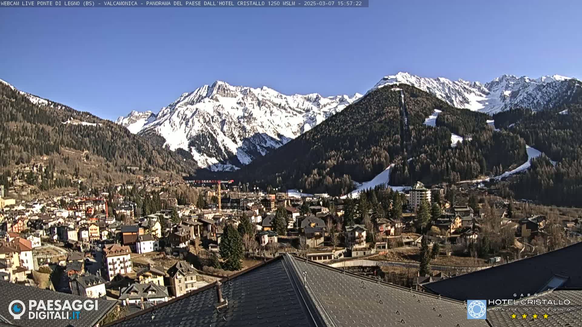 A sunny view of a snow-capped mountain range overlooking a town nestled in a valley.