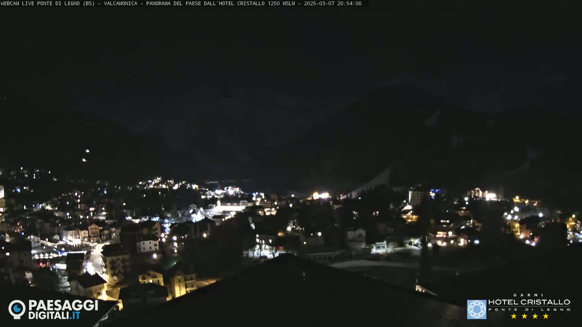 A nighttime view of a town nestled in a valley, with mountains in the background under a clear, dark sky.