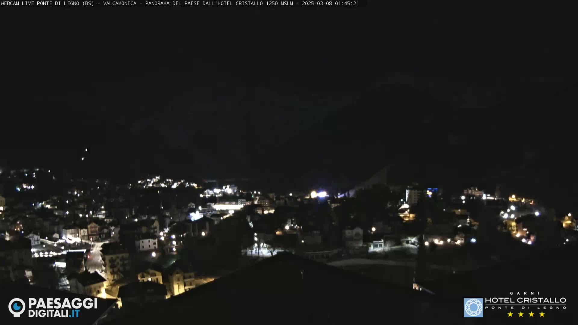 A nighttime, aerial view of a town nestled in a valley, illuminated by scattered lights.