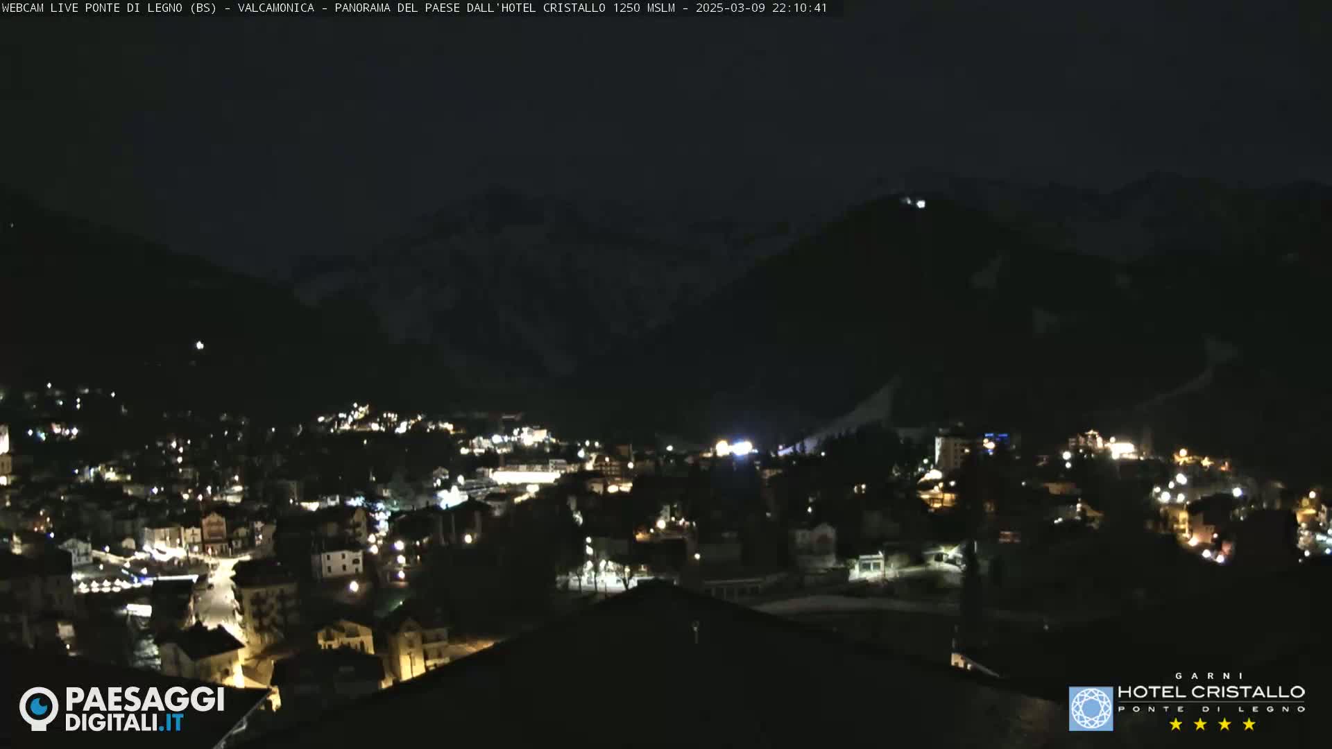 A nighttime view of a town nestled in a valley between snow-capped mountains.