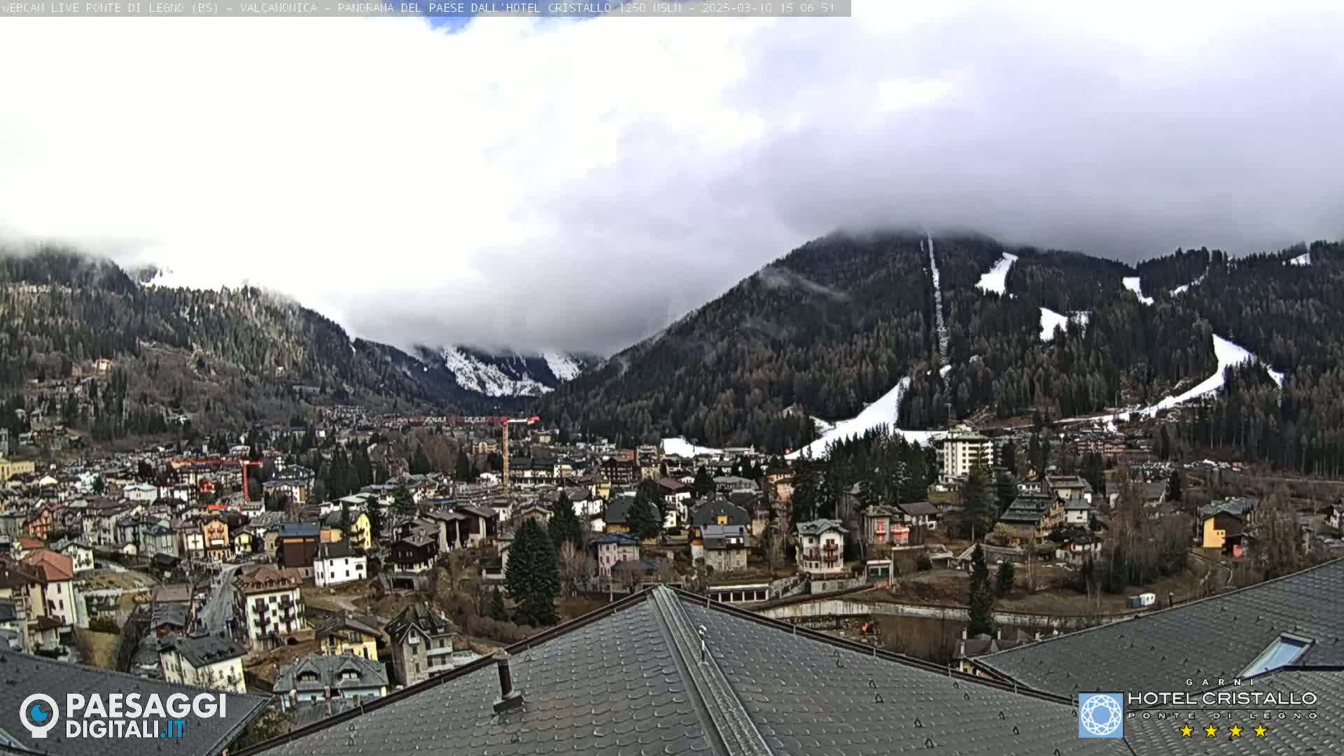 A mountain town nestled in a valley, partially obscured by clouds, with snow-covered slopes visible in the background.