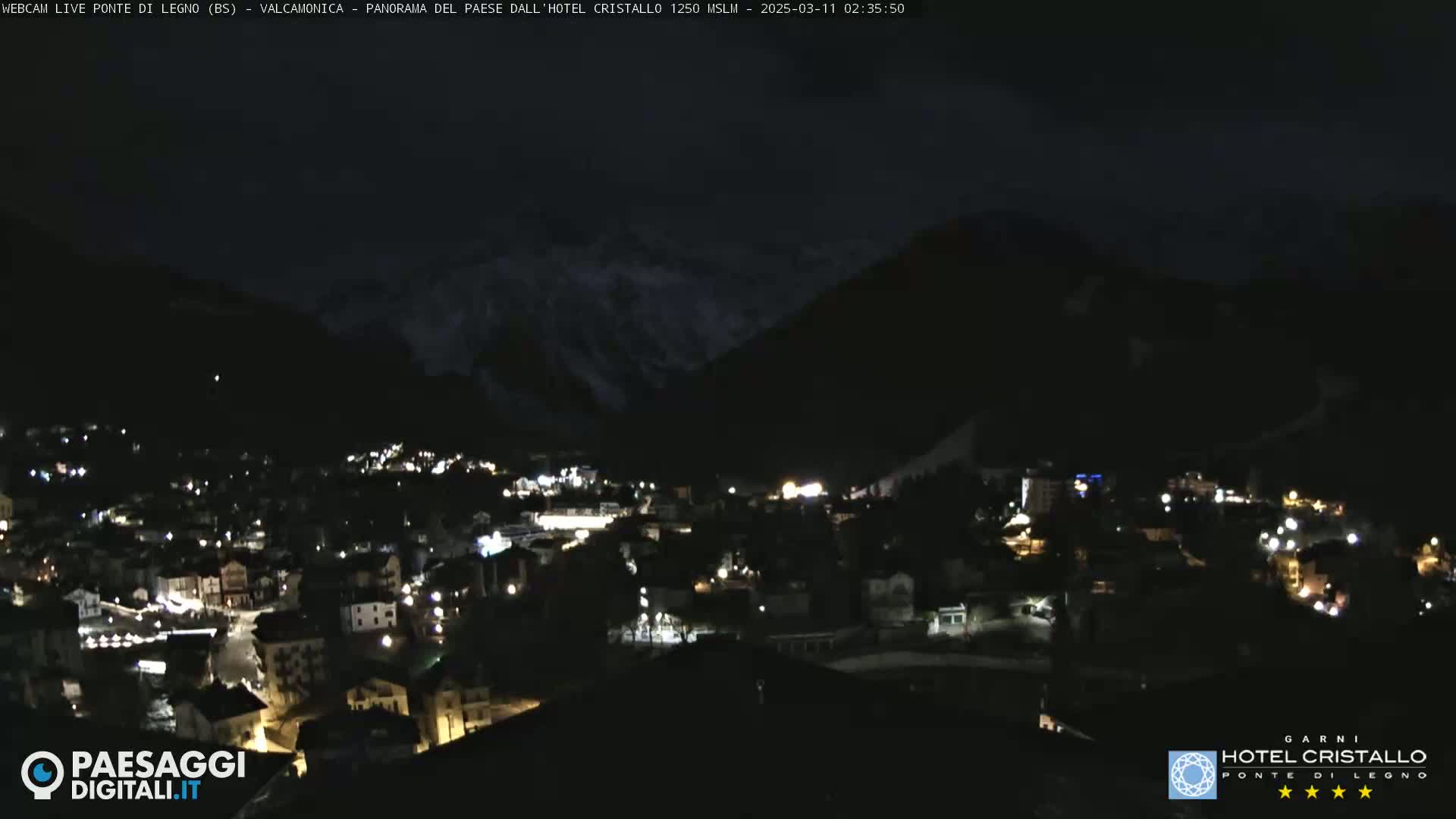A nighttime view of a town nestled in a valley, surrounded by dark mountains under a mostly clear sky.