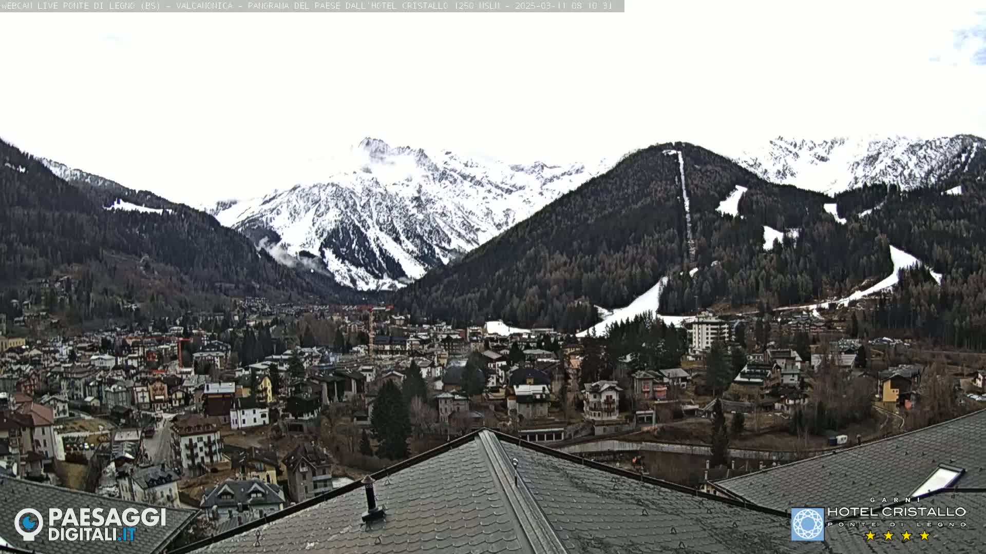 A snow-dusted mountain range overlooks a town nestled in a valley, with overcast skies.