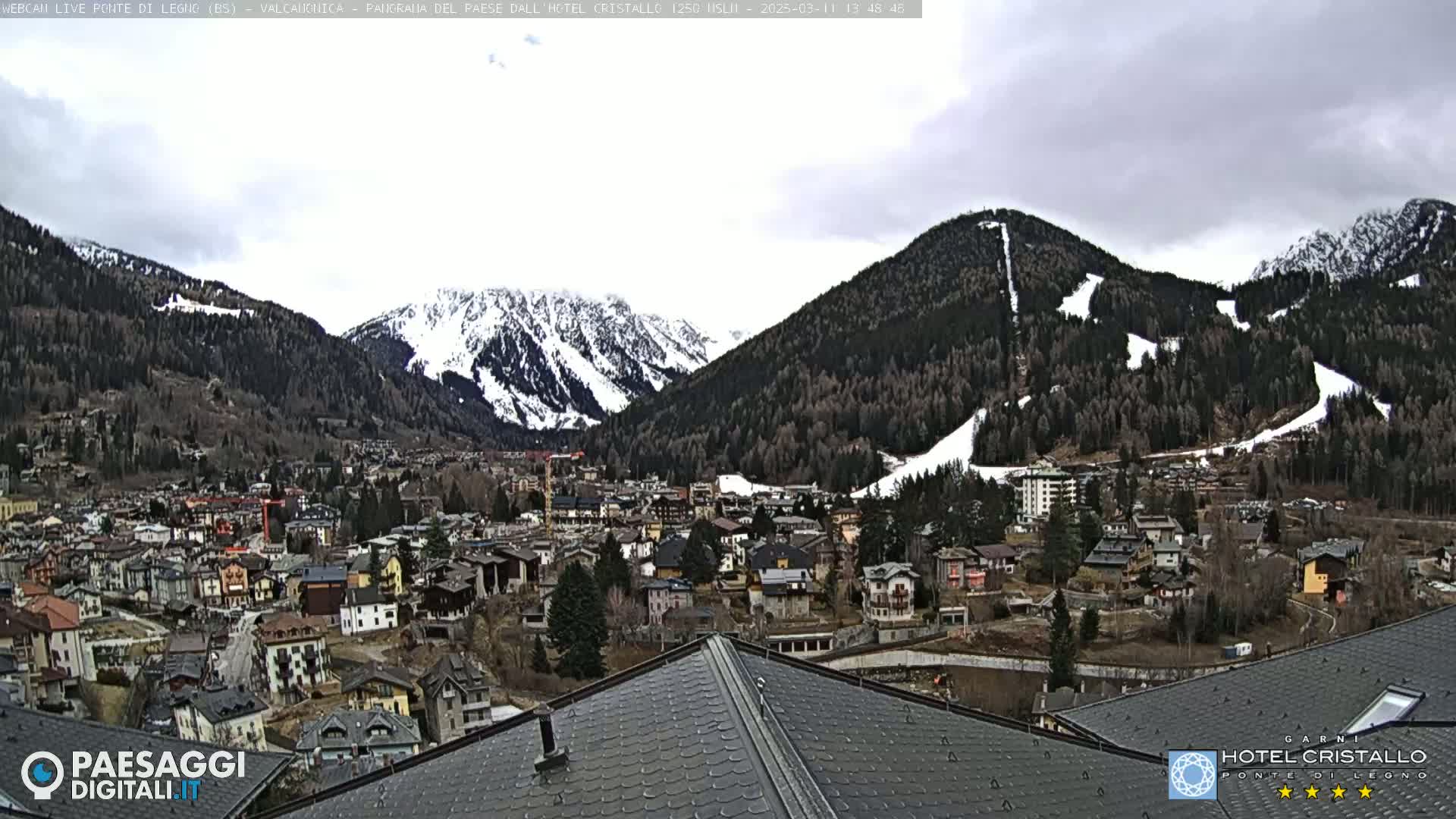 A mountain town nestled in a valley between snow-capped mountains under an overcast sky.