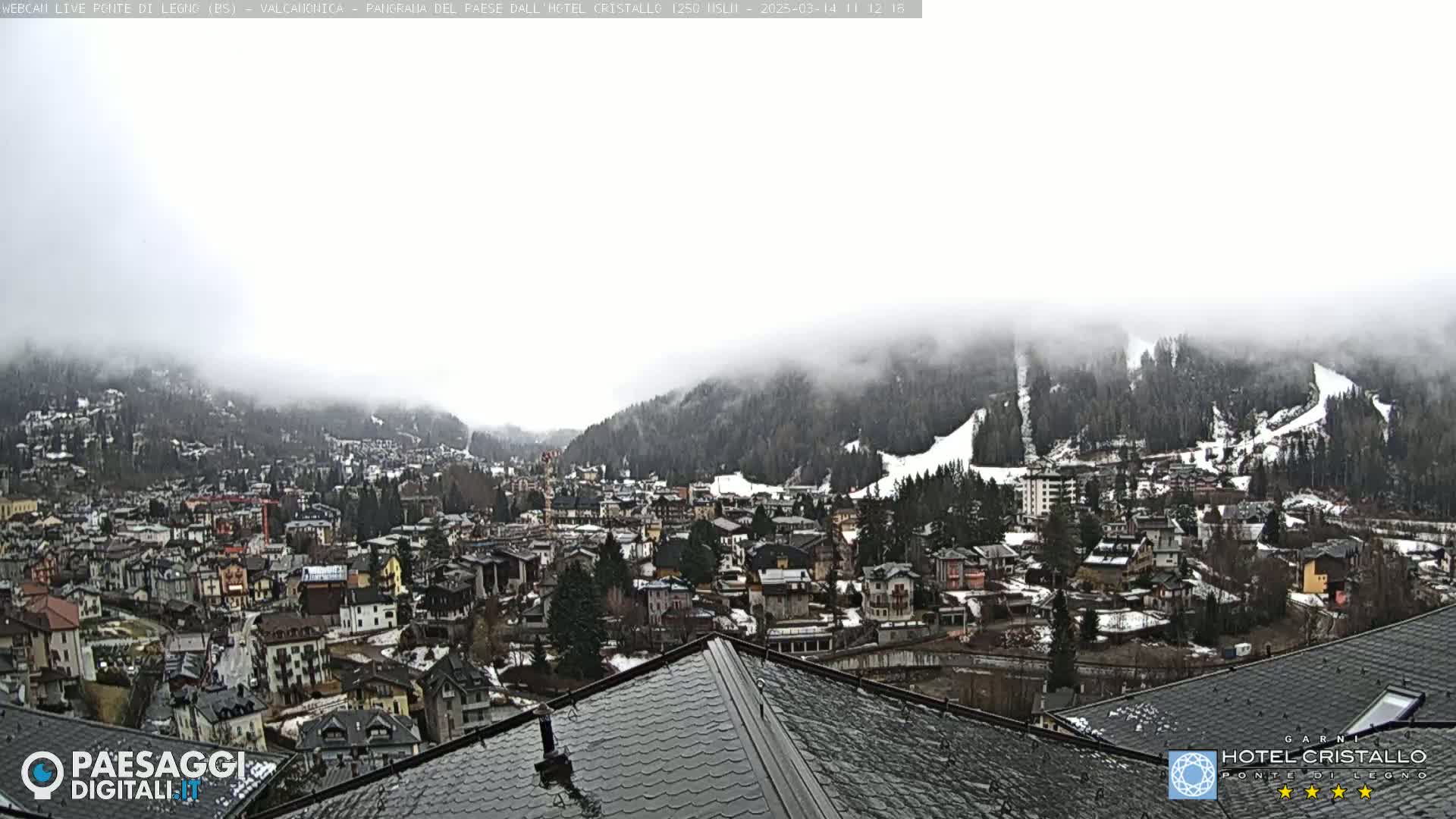 A foggy mountain town with snow-covered slopes is viewed from a rooftop.