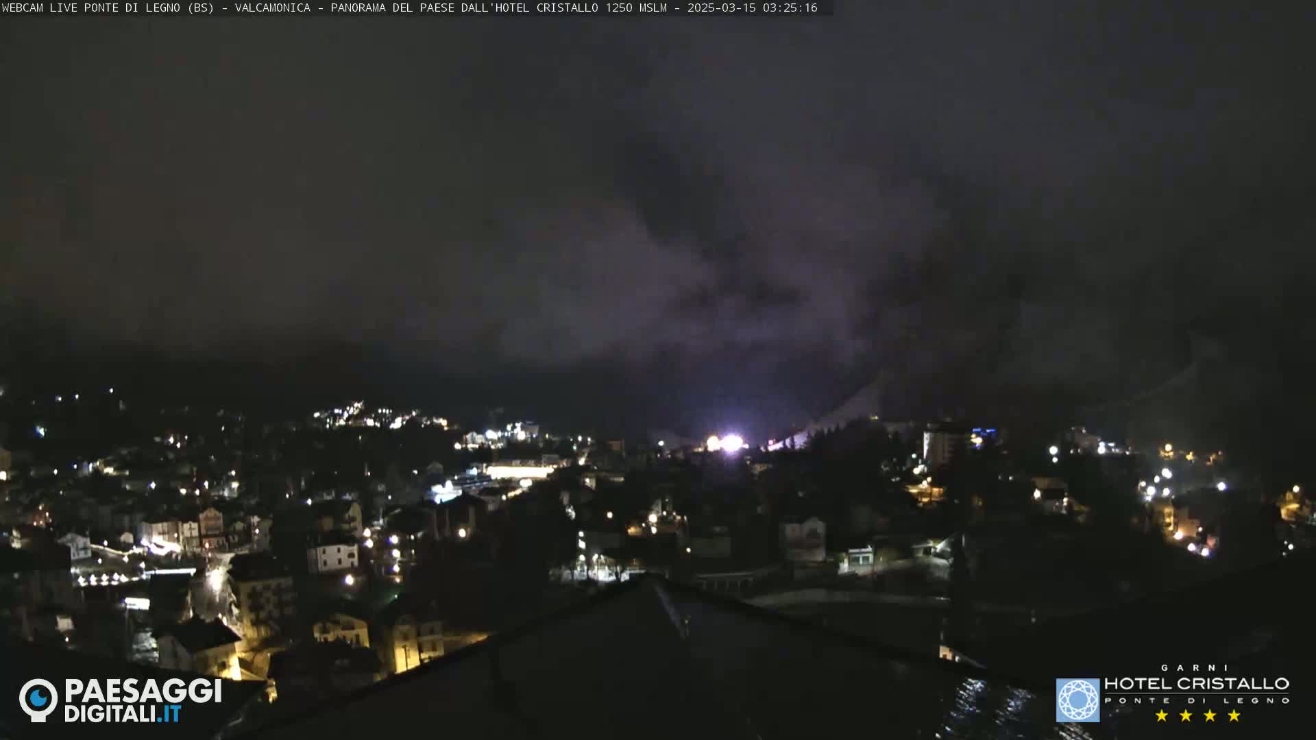 A nighttime view of a town nestled in a valley, shrouded in fog or low clouds.