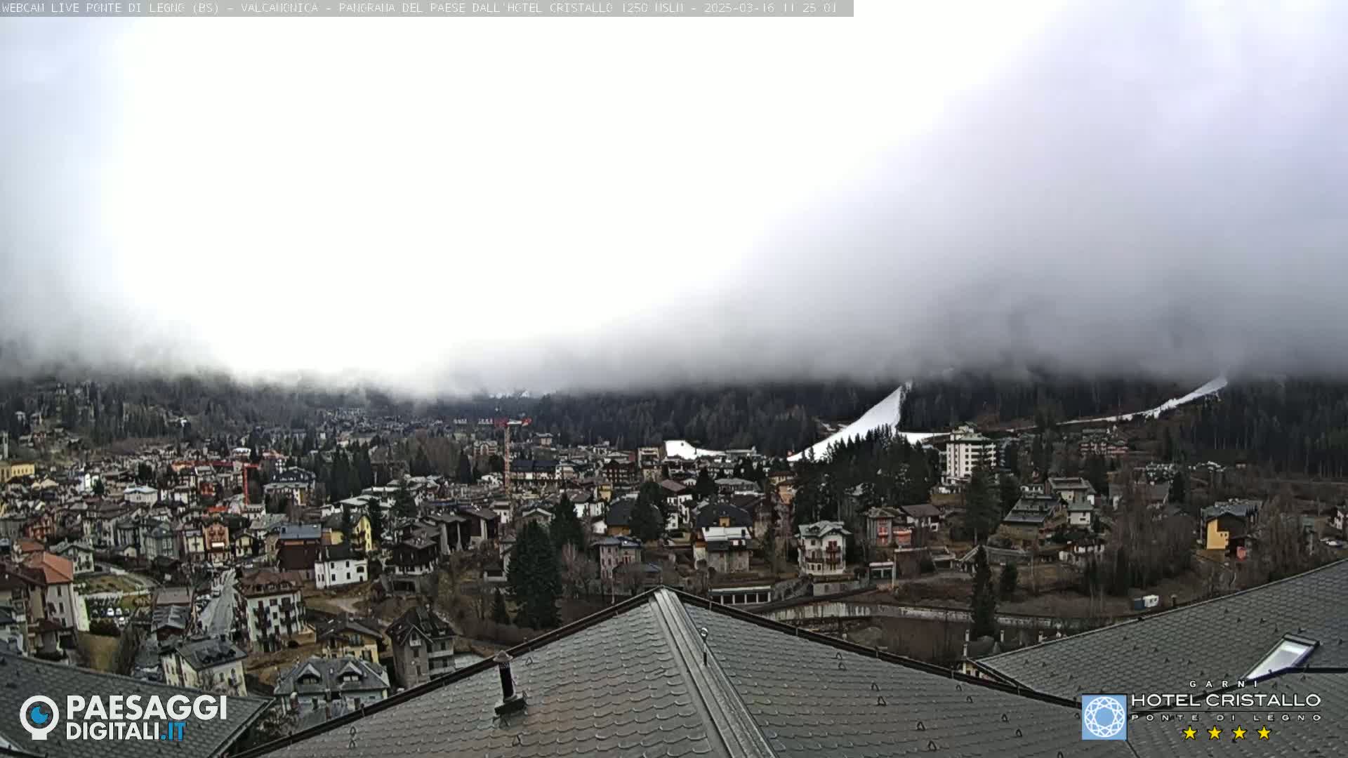 A foggy day reveals a town nestled in a valley, with snow-covered hills in the background.