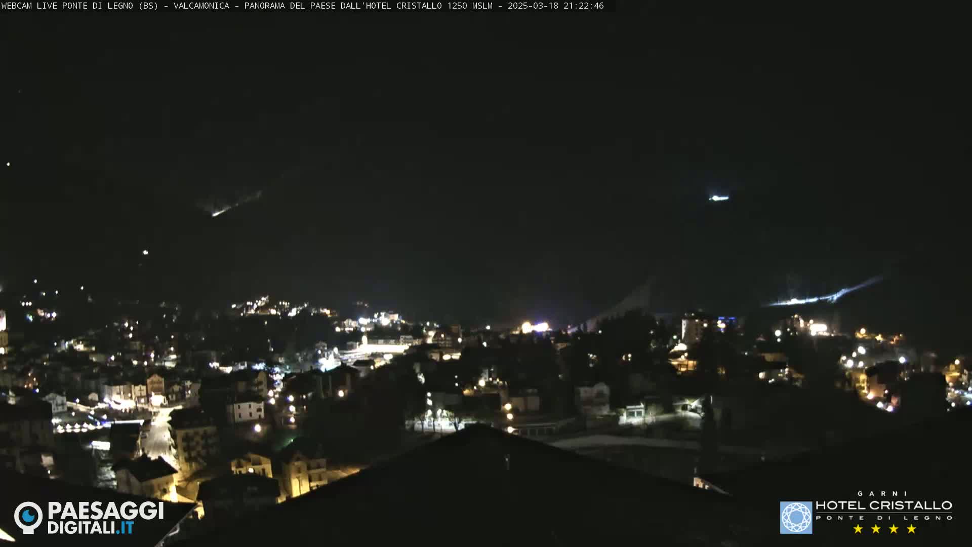 A nighttime view of a town nestled in a valley, illuminated by scattered lights under a clear, dark sky.