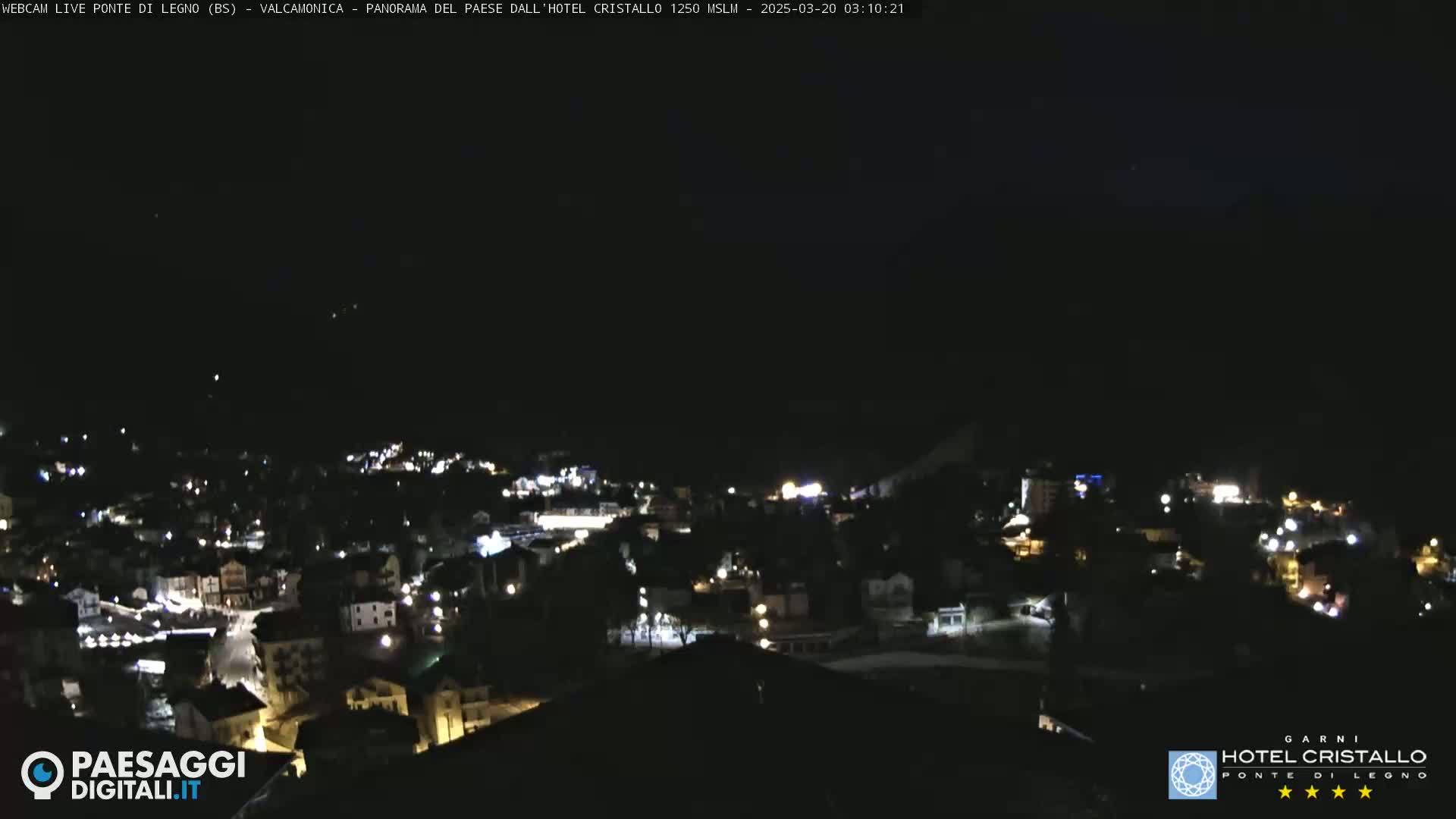 A nighttime, long shot of a town illuminated by scattered lights under a clear, dark sky.