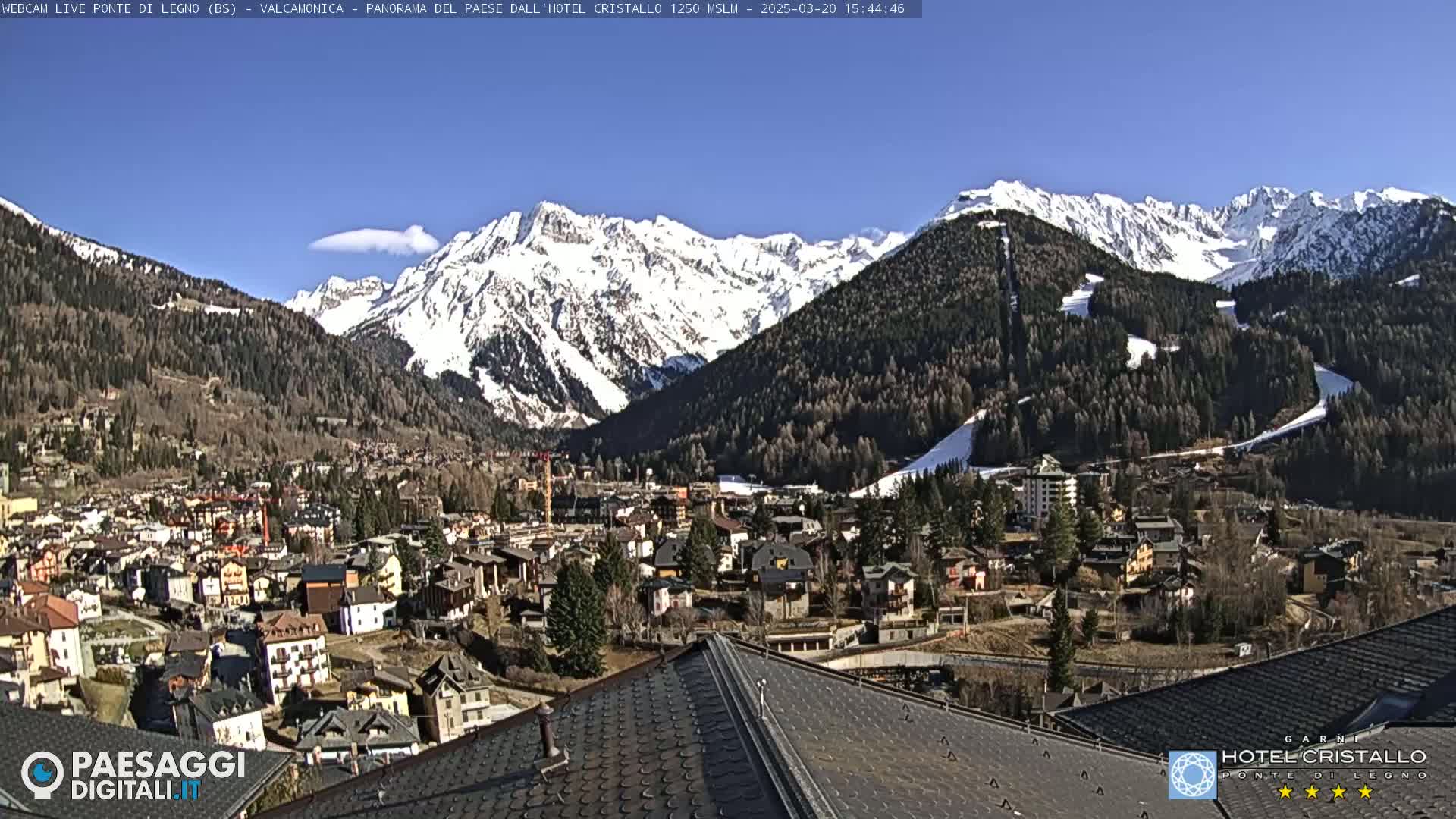 A sunny, snow-capped mountain range overlooks a town nestled in a valley.