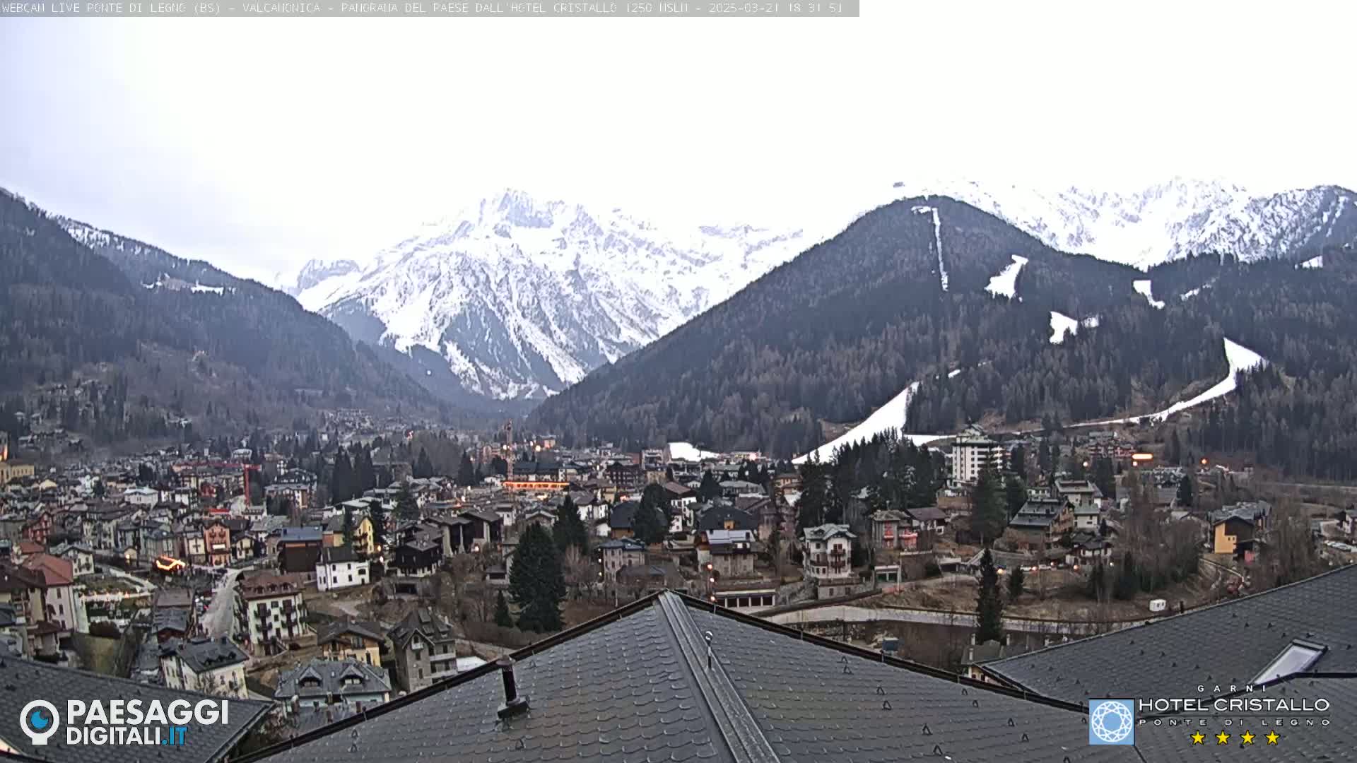 A mountain town nestled in a valley, overlooked by snow-capped mountains under an overcast sky.