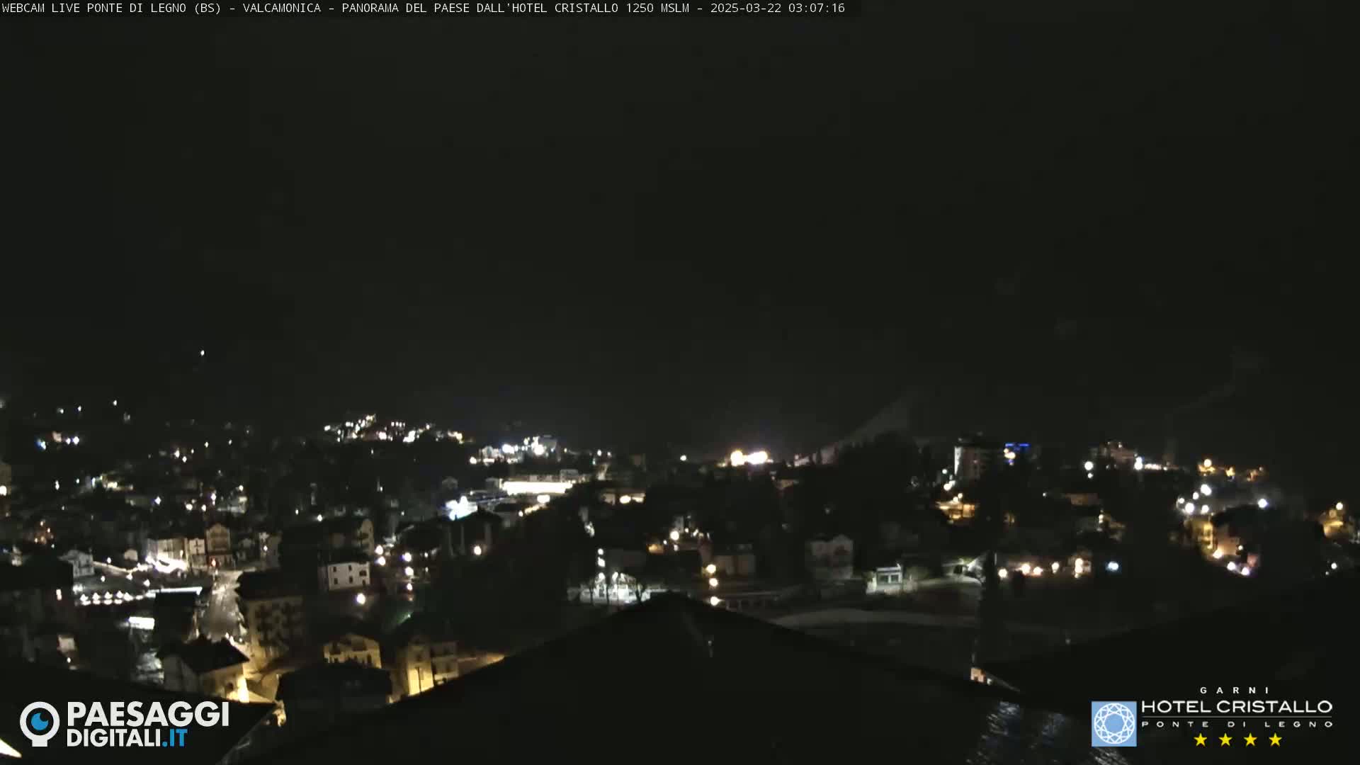 A nighttime view of a town nestled in a valley, with the lights of buildings scattered across the landscape under a dark sky.