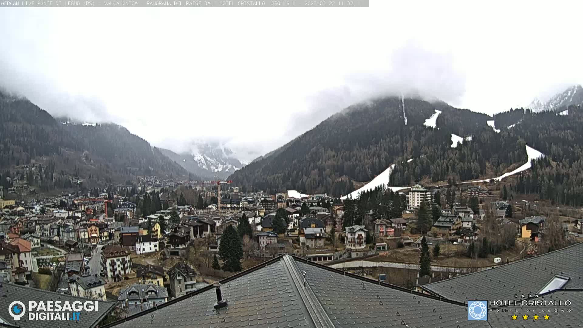 A mountain town nestled in a valley, partially obscured by fog, with snow visible on the surrounding hills.