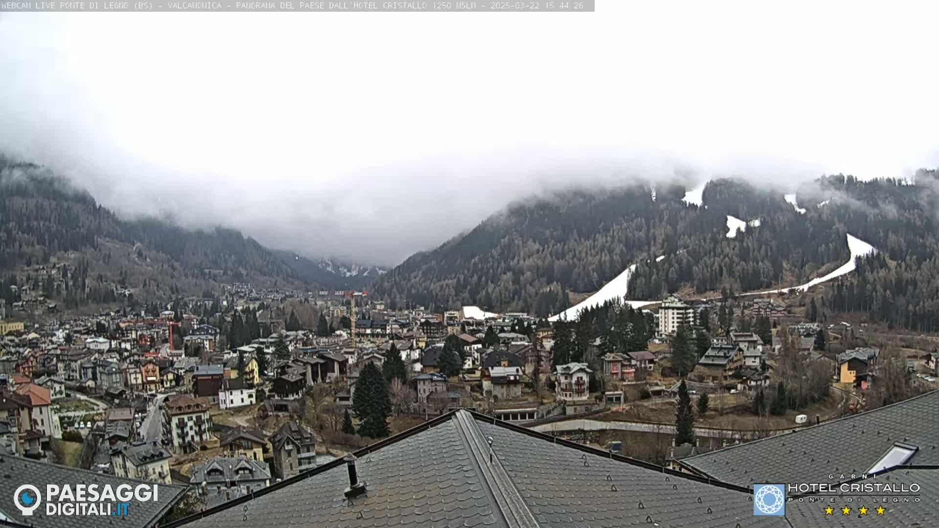 A mountain town nestled in a valley, partially shrouded in fog, with snow visible on the surrounding hillsides.