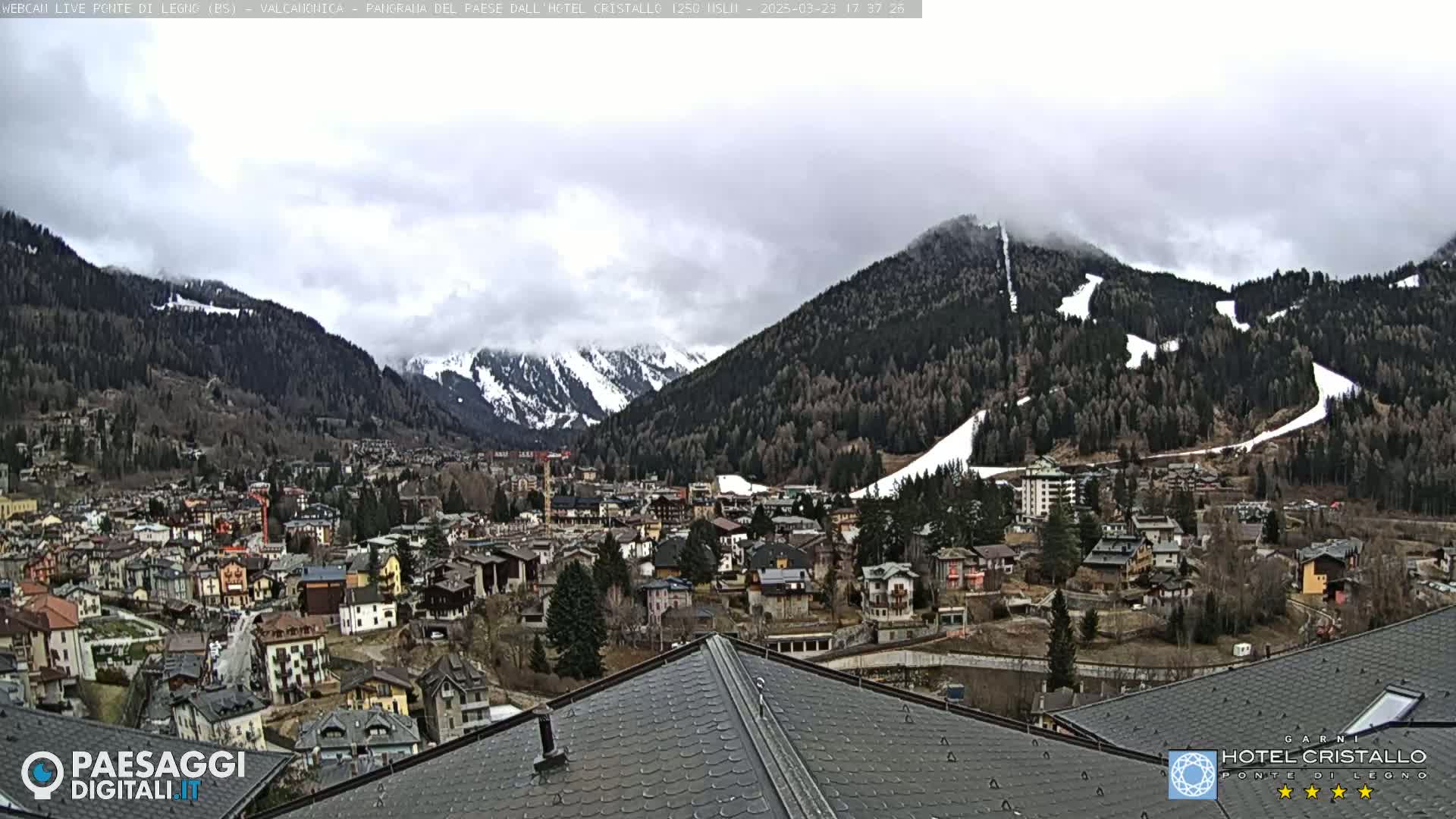 A mountain town nestled in a valley, partially covered in snow, under a cloudy sky.