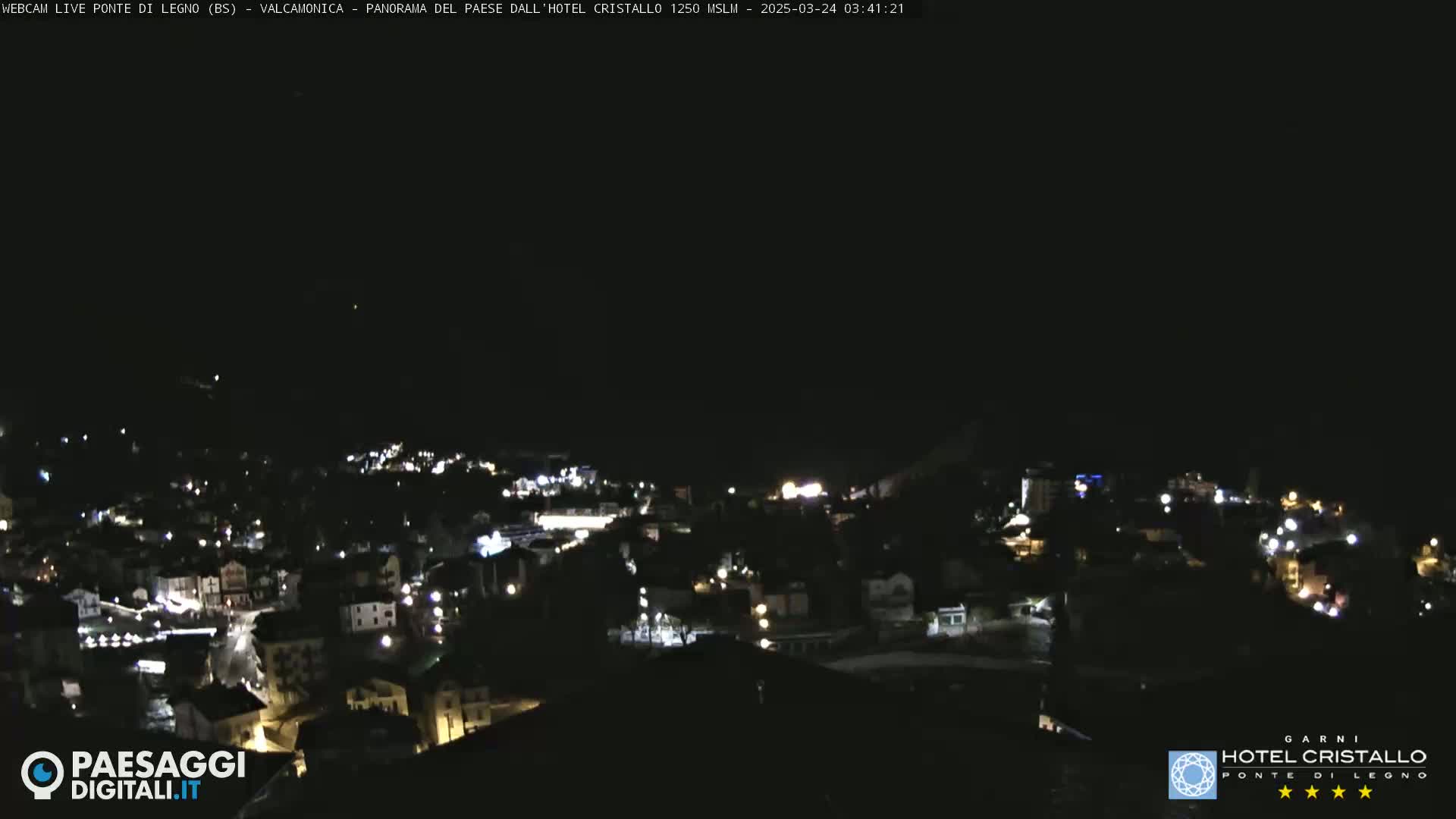 A nighttime, long shot of a town illuminated by scattered lights under a clear, dark sky.