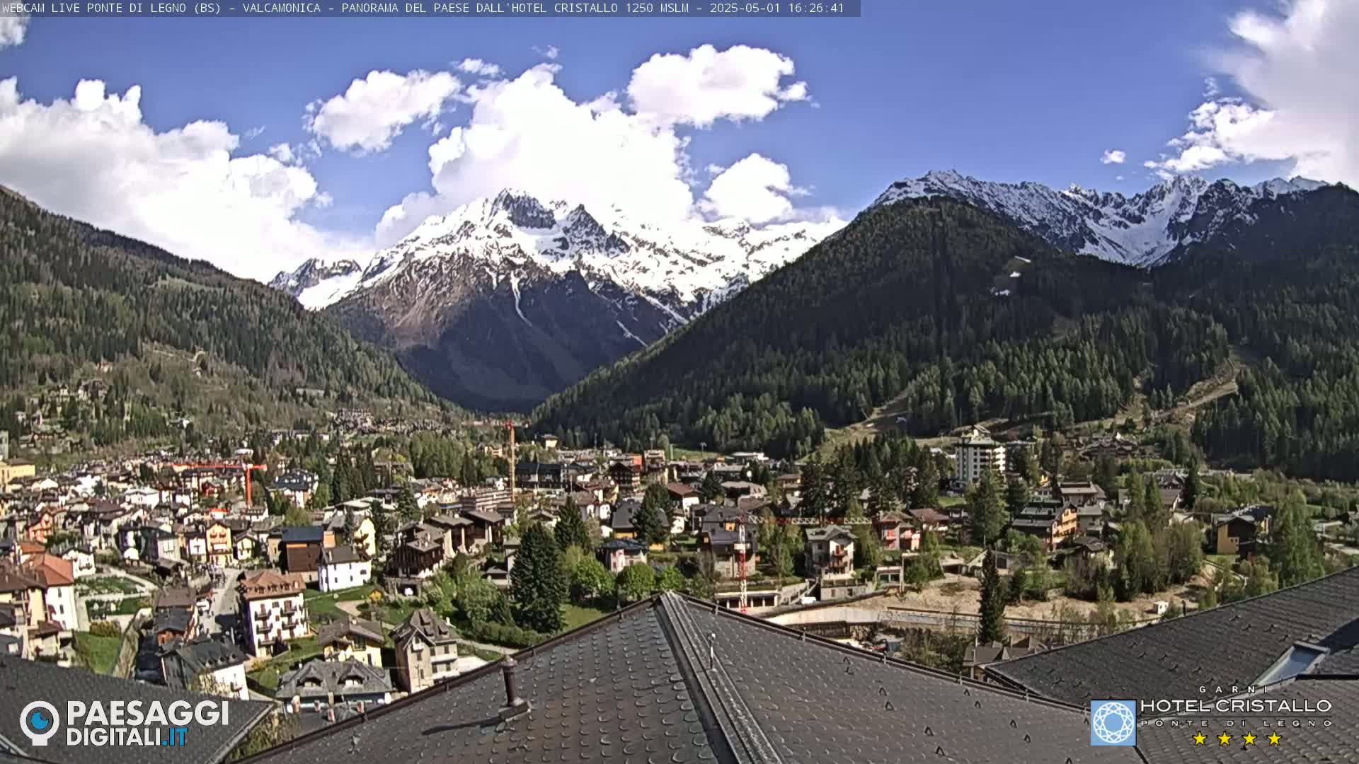A partially cloudy day reveals a snow-capped mountain range overlooking a town nestled in a valley.