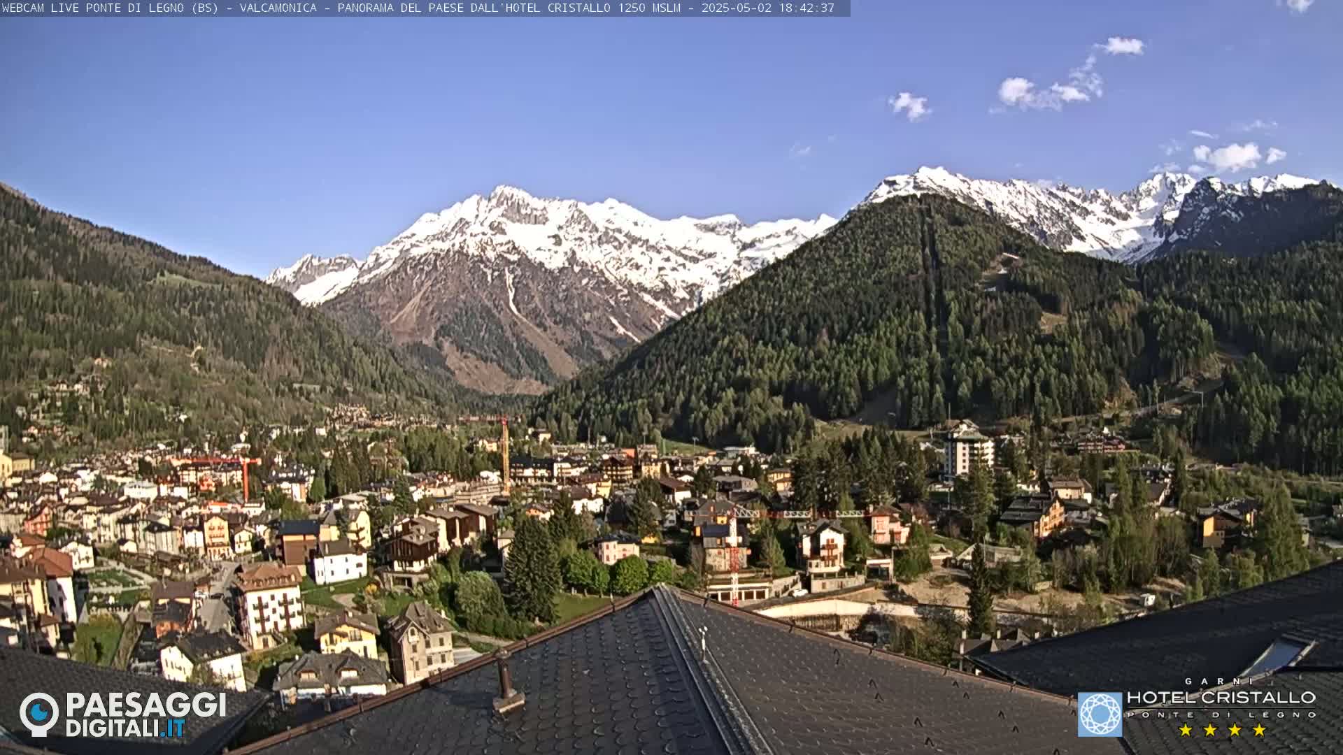 A mountain town nestled in a valley, with snow-capped mountains in the background under a clear blue sky.