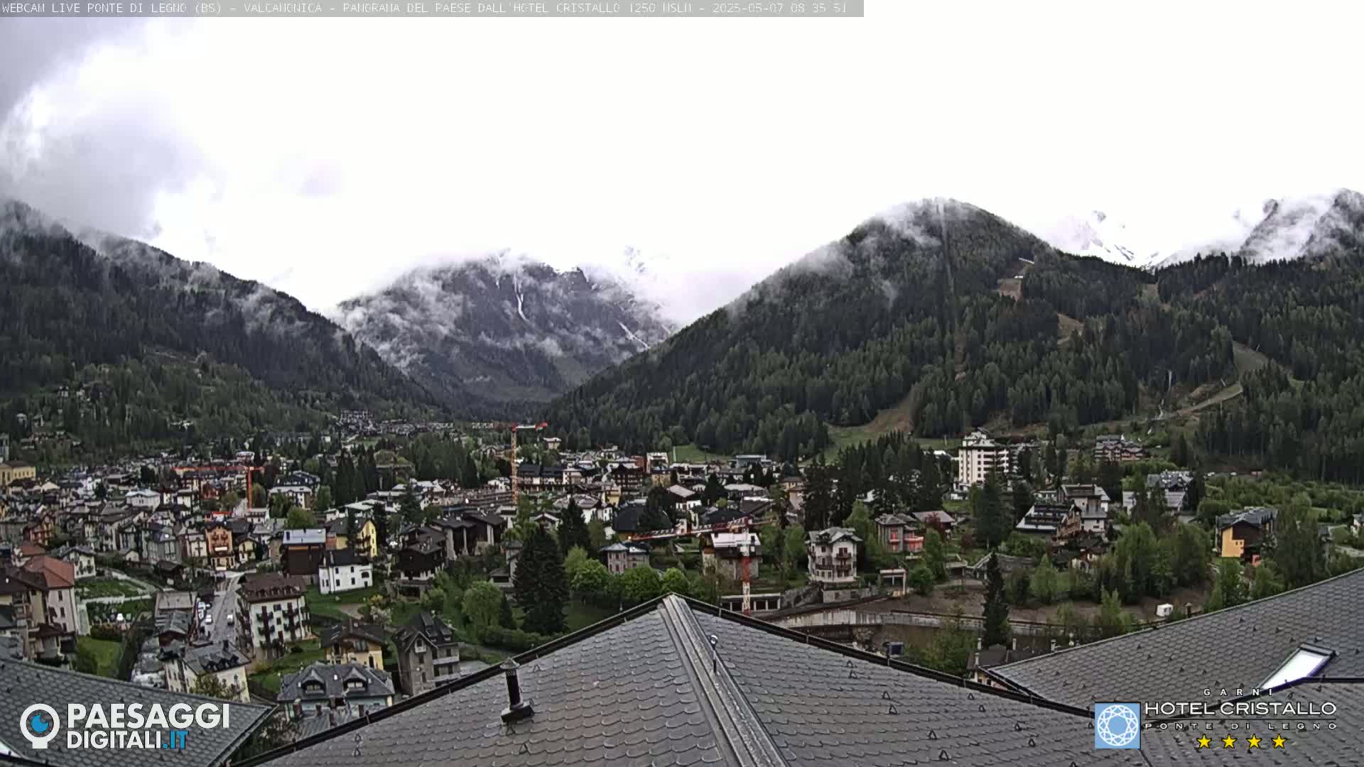 A mountain town nestled in a valley, partially obscured by fog and low clouds, sits below snow-capped mountains.